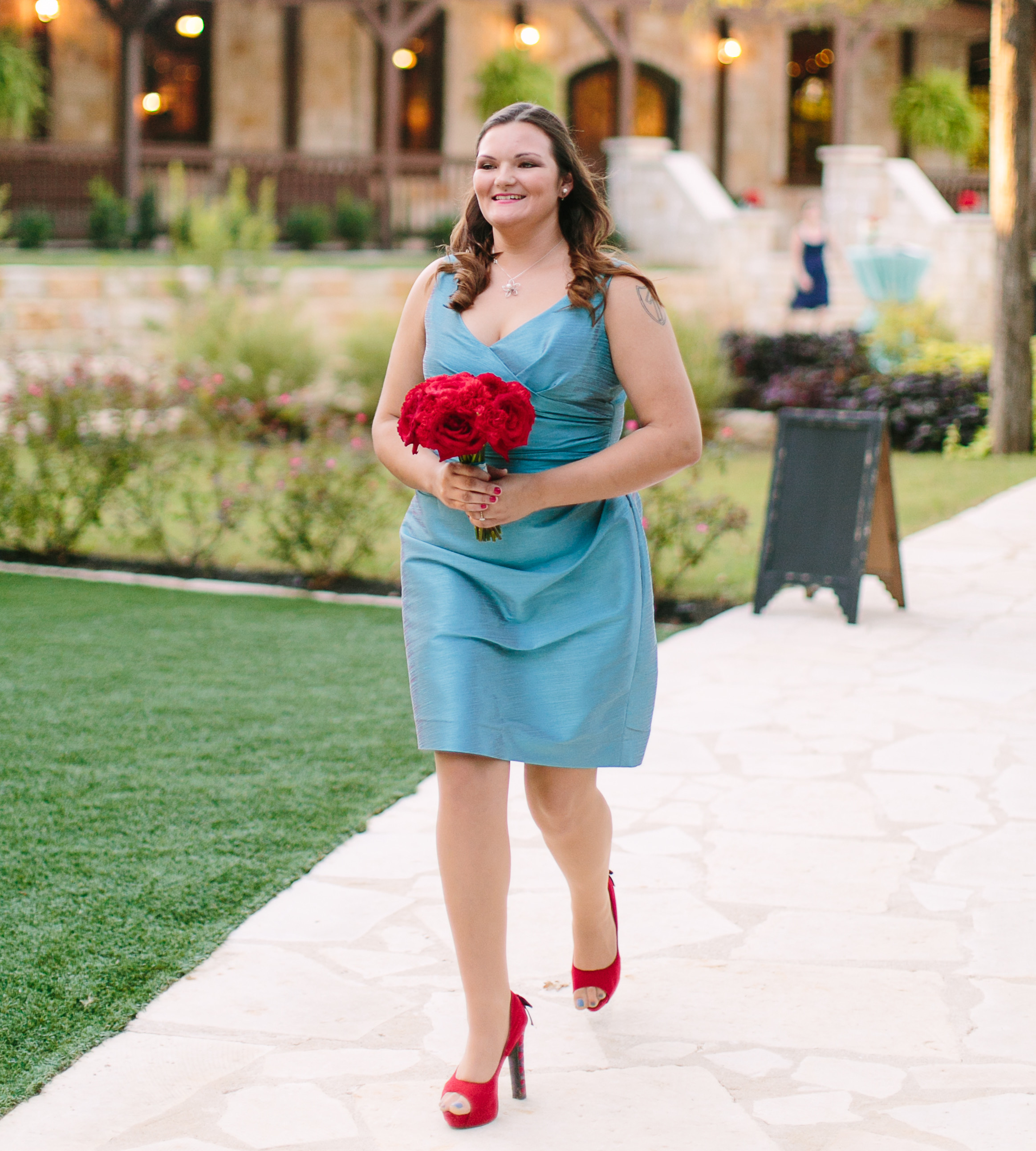 A Bridesmaid walks down the aisle wearing a teal dress and red shoes