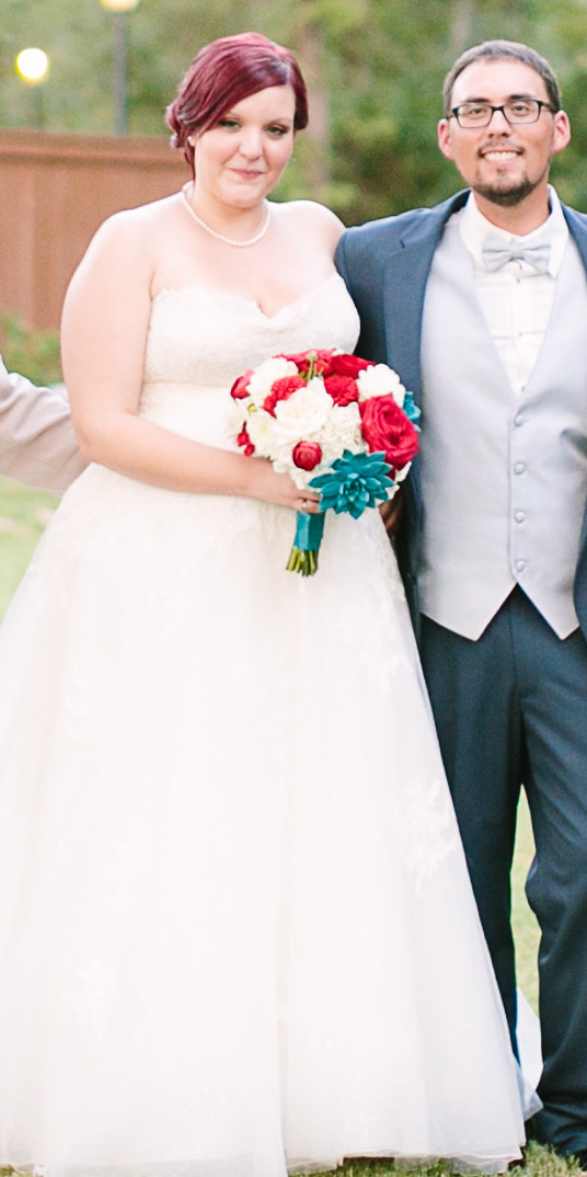 A bride carrying a red and teal bouquet and her new husband embrace