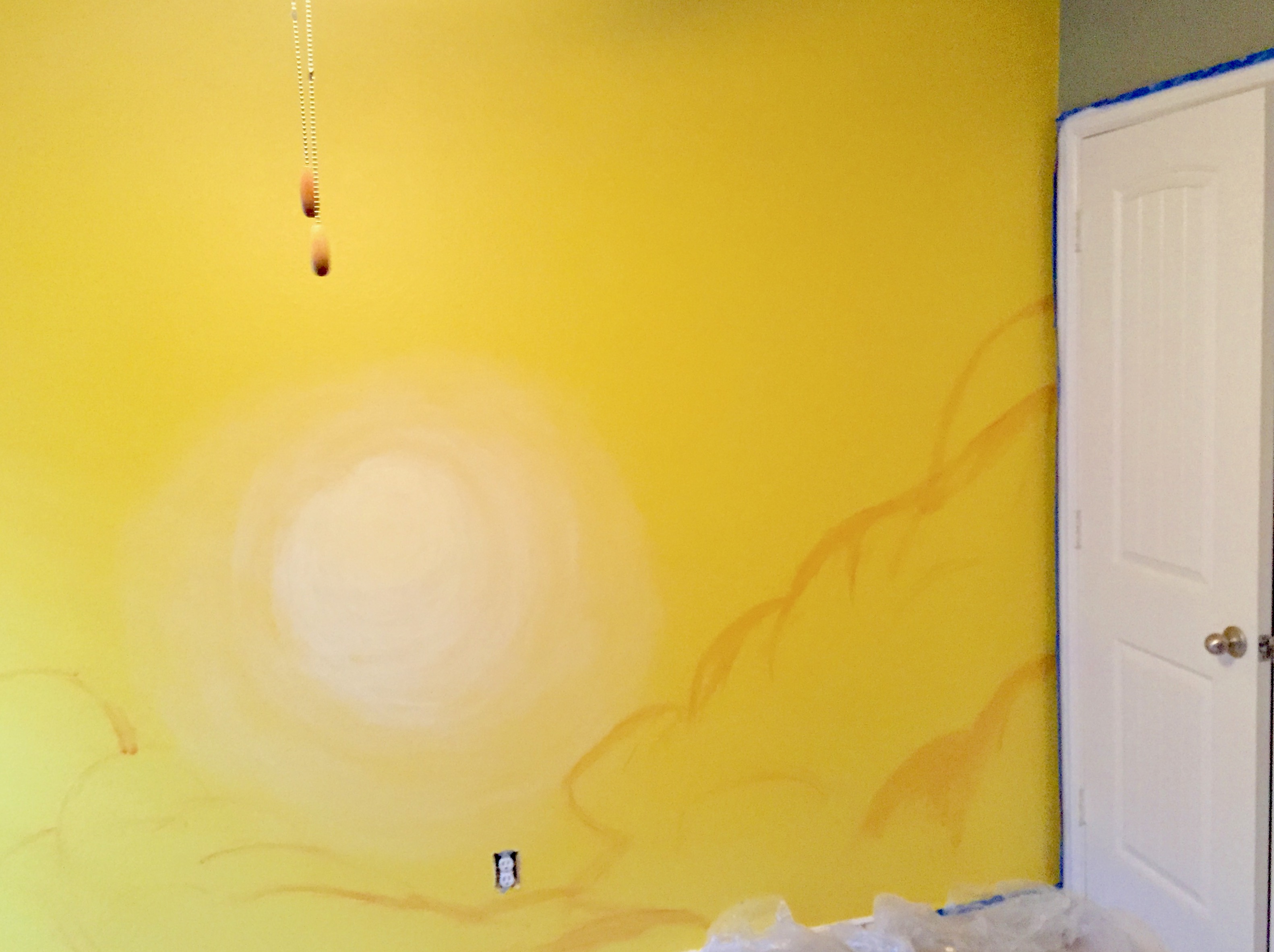 A painted pale yellow circular sun and the outline of orange clouds on a yellow wall