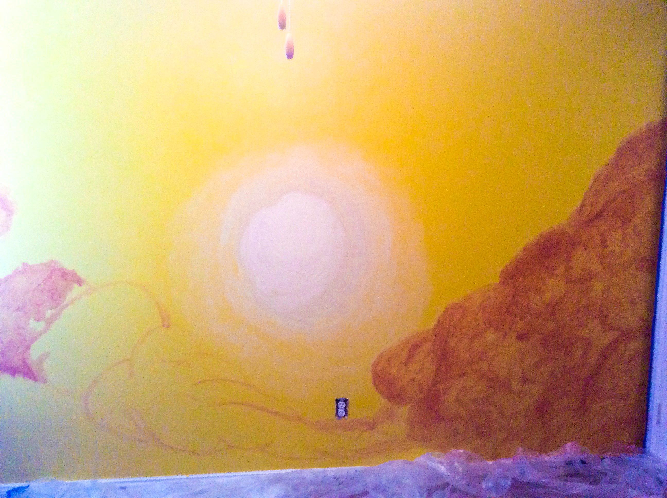 A pale yellow circular sun and partially shaded orange clouds on a yellow wall 