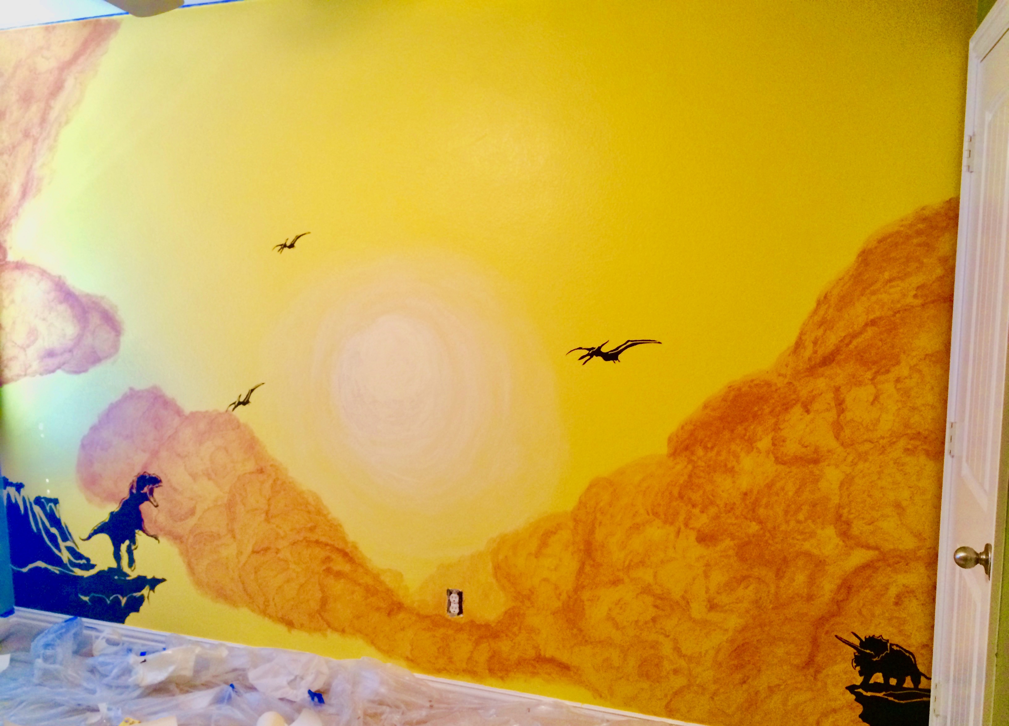 A yellow mural with orange clouds, a pale yellow sun, and black vinyl dinosaurs