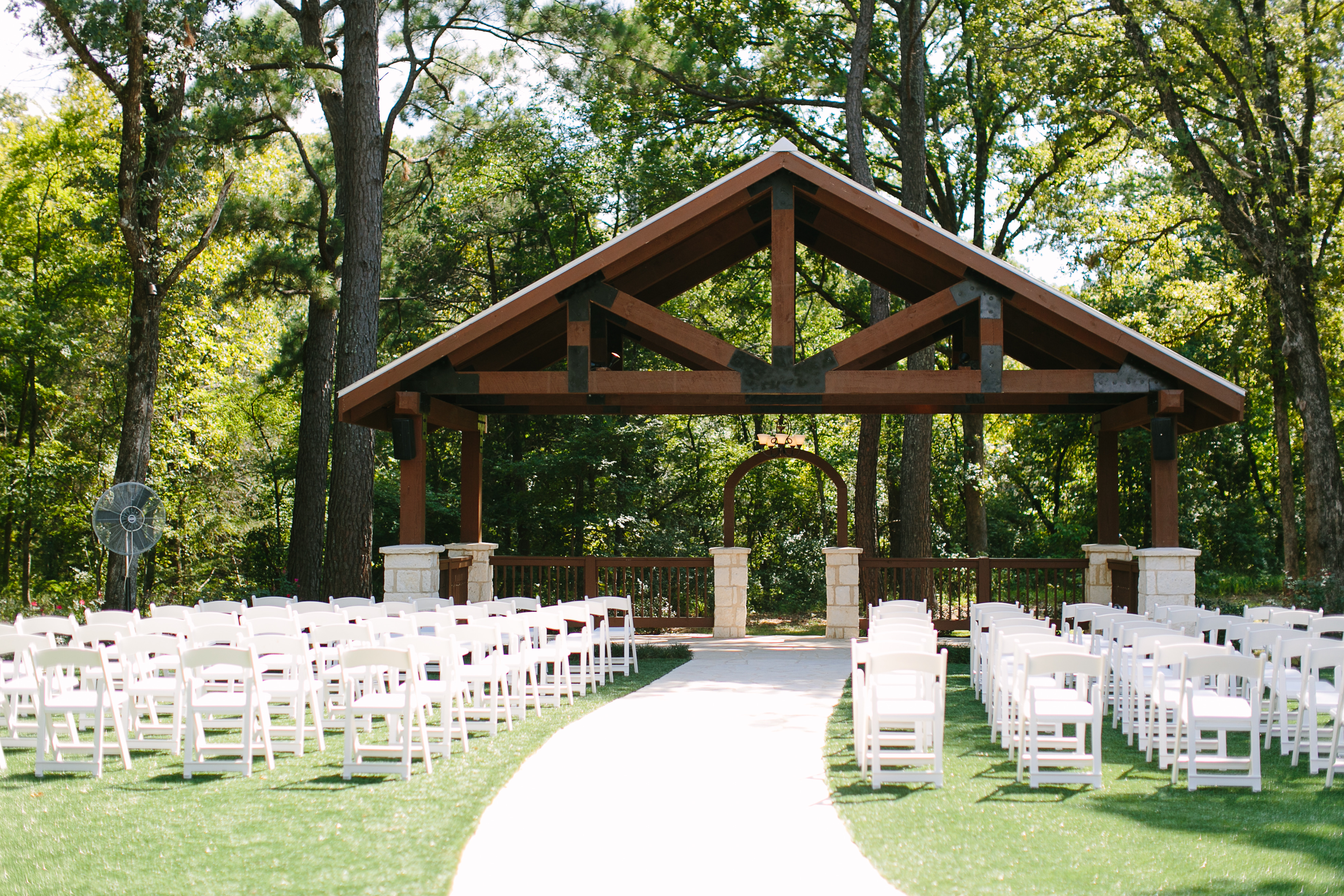 An outdoor wedding venue with white chairs and a wood arbor
