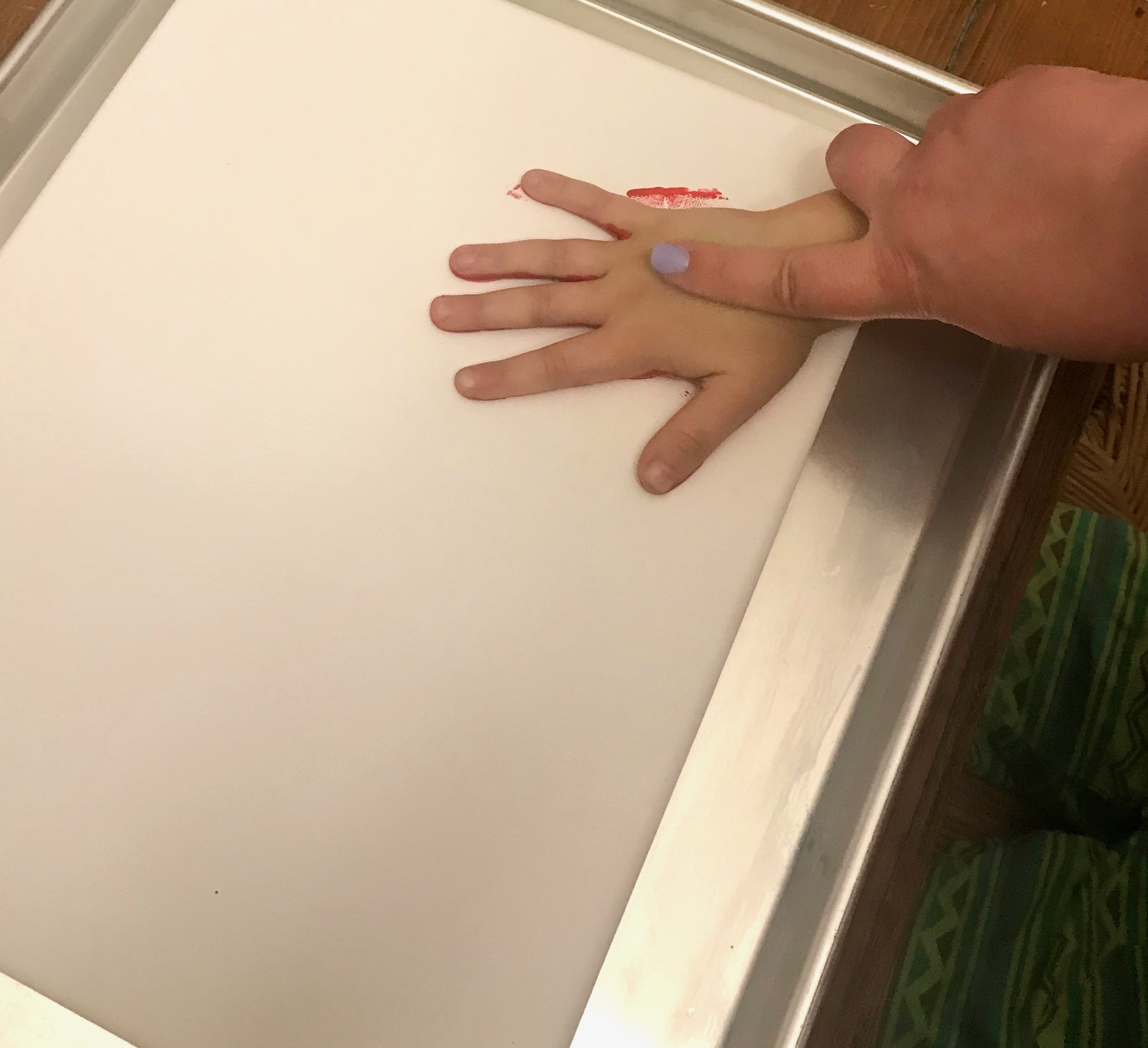 A parent's hand pressing a painted child's hand onto blank canvas. 