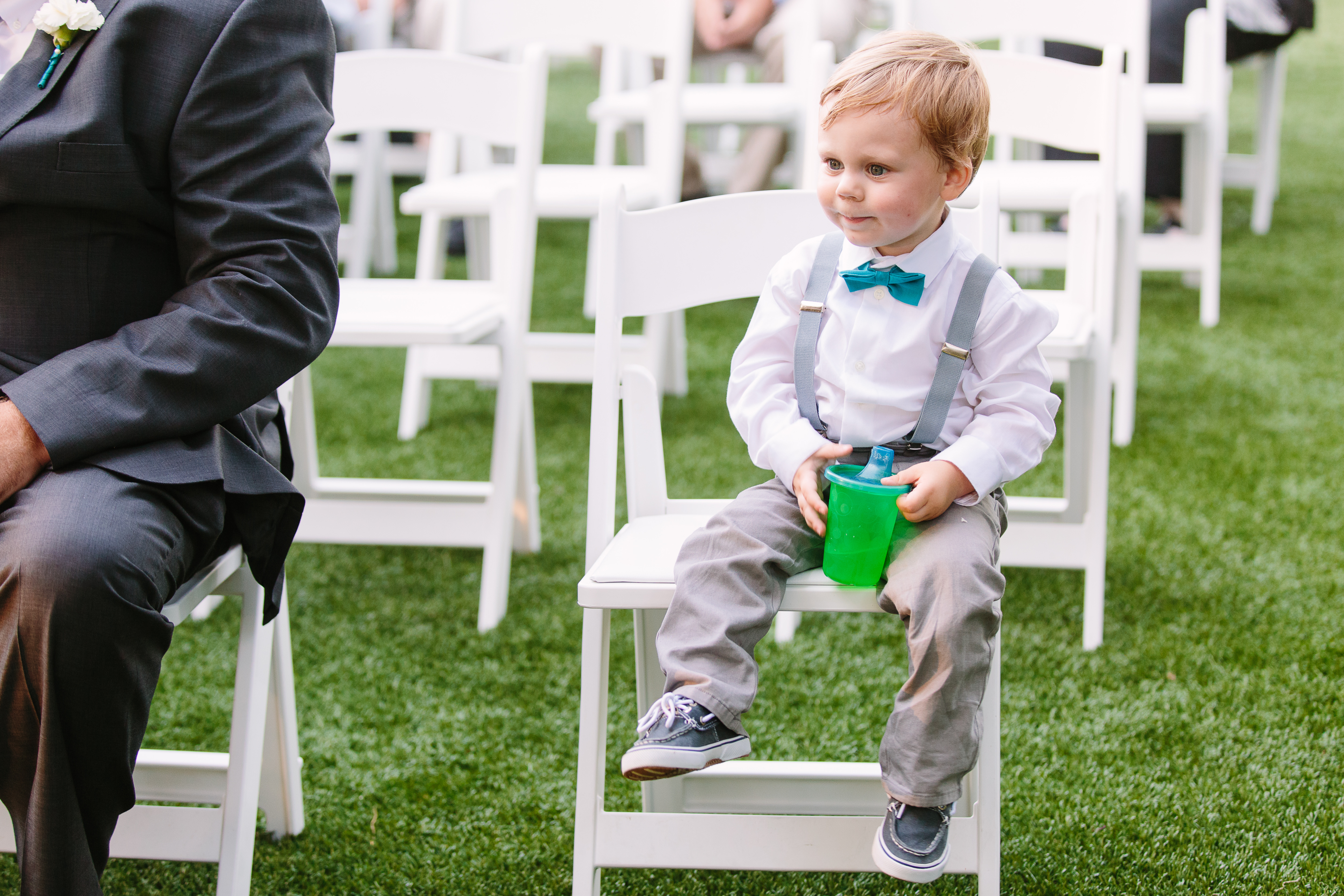 A toddler sits in a white wedding venue chair holding a green sippy cup