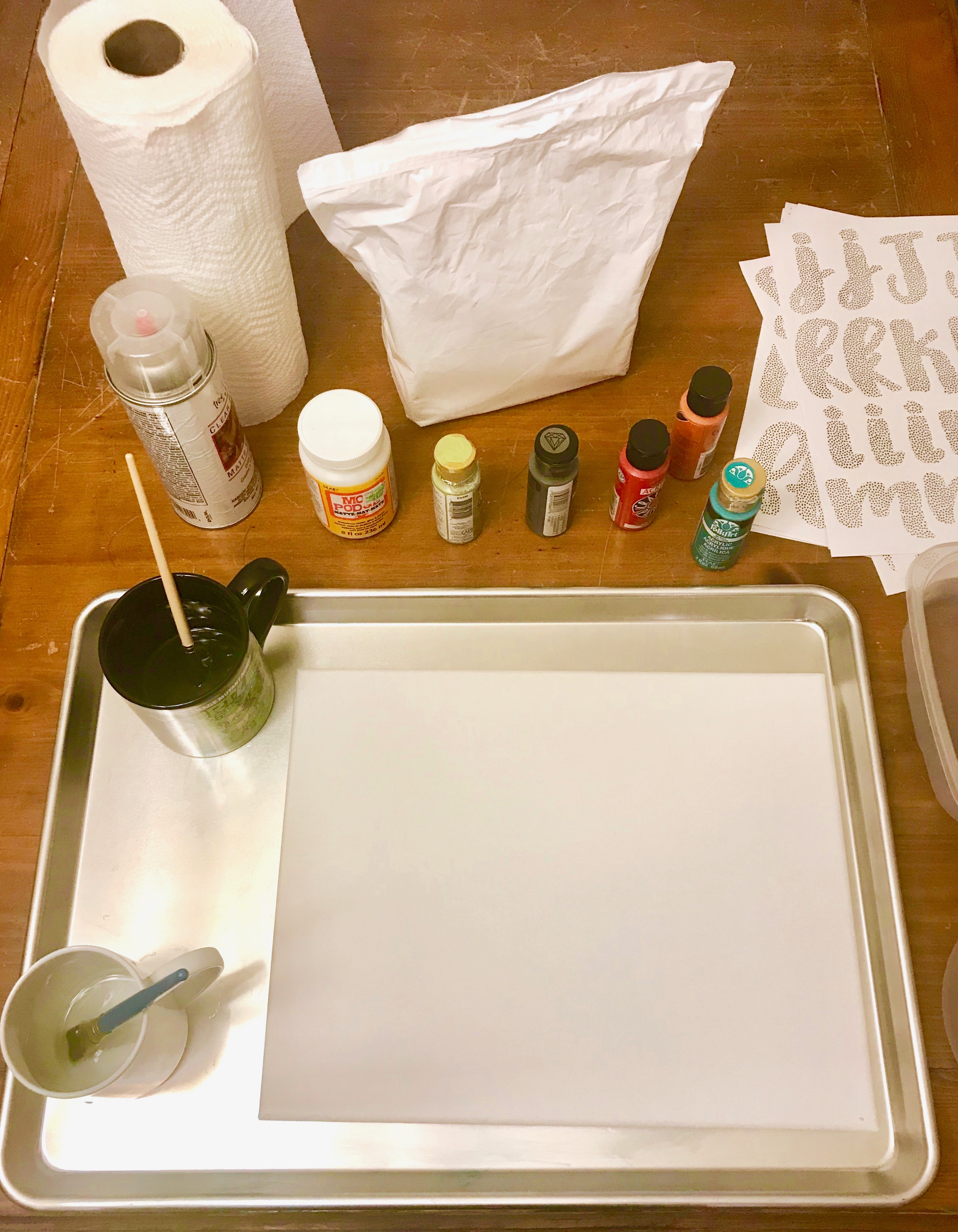 Crafting supplies including canvas, paint, and mod podge on a wood table