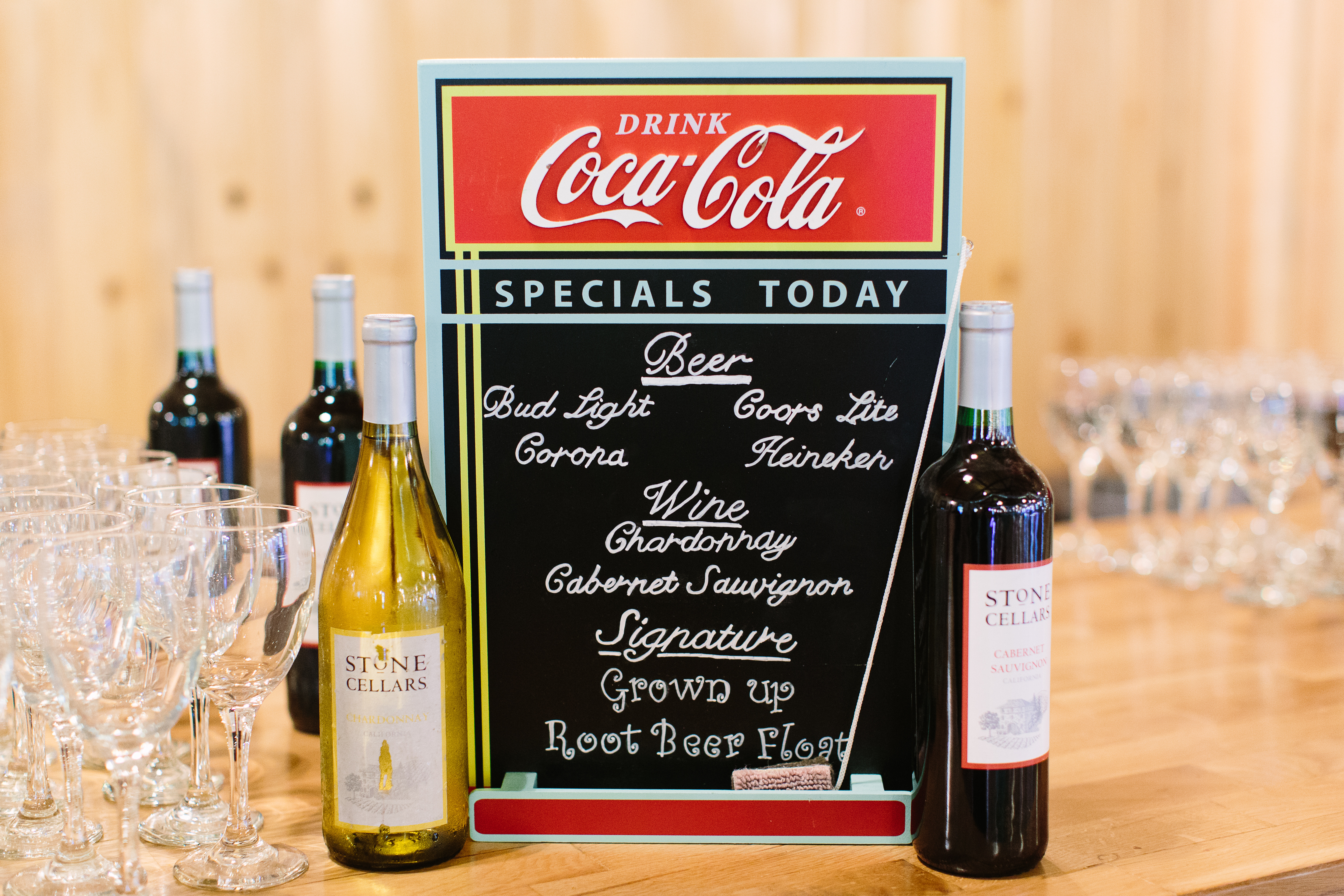 Bottles of wine, wine glasses, and a chalkboard menu on a wooden bar counter