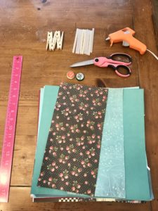 Crafting supplies including scrapbook paper, a ruler, and scissors on a wood table