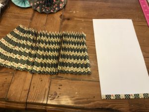 A folded piece of patterned scrapbook paper next to a piece being folded. 