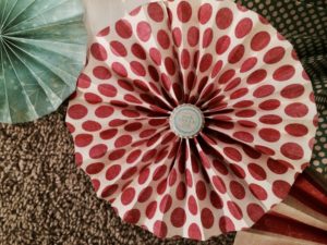 A red polka-dotted paper pinwheel with a bottle cap in the center.