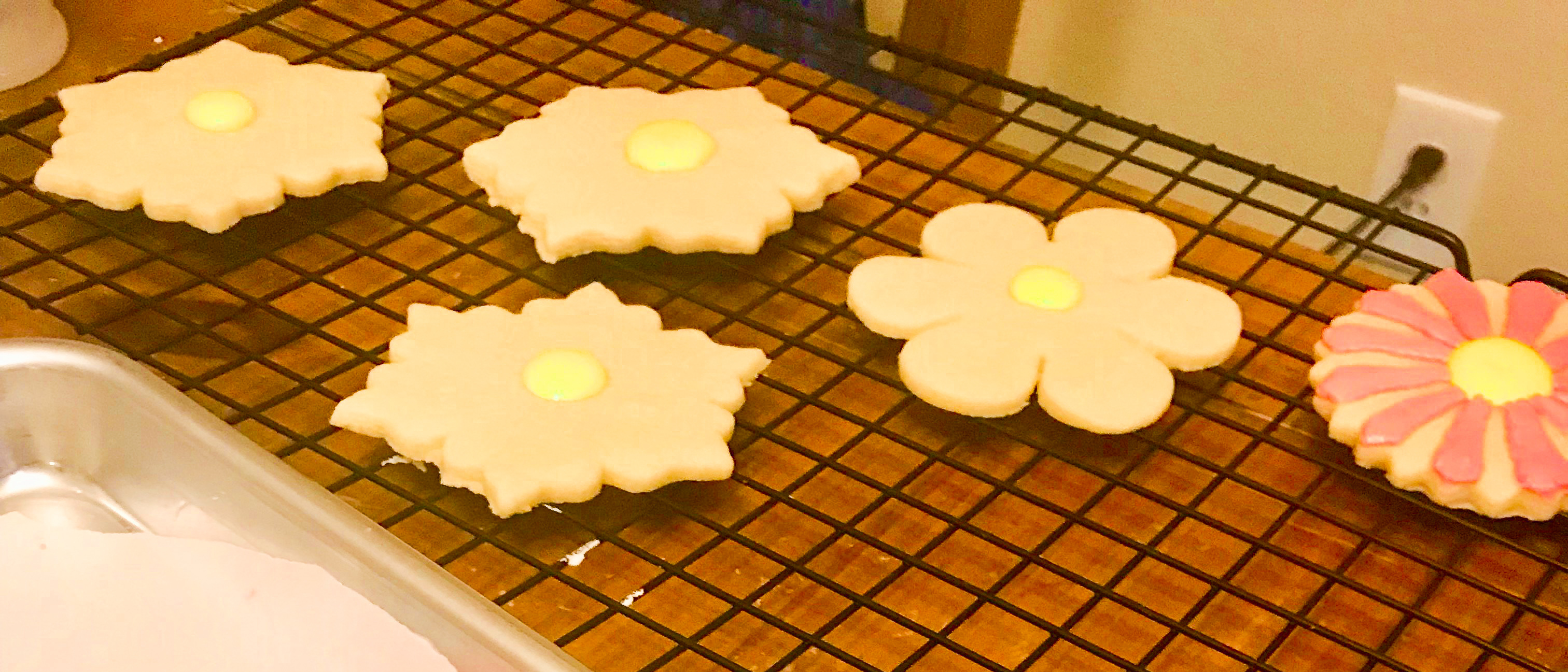 Partially decorated flower cookies on a cooling rack
