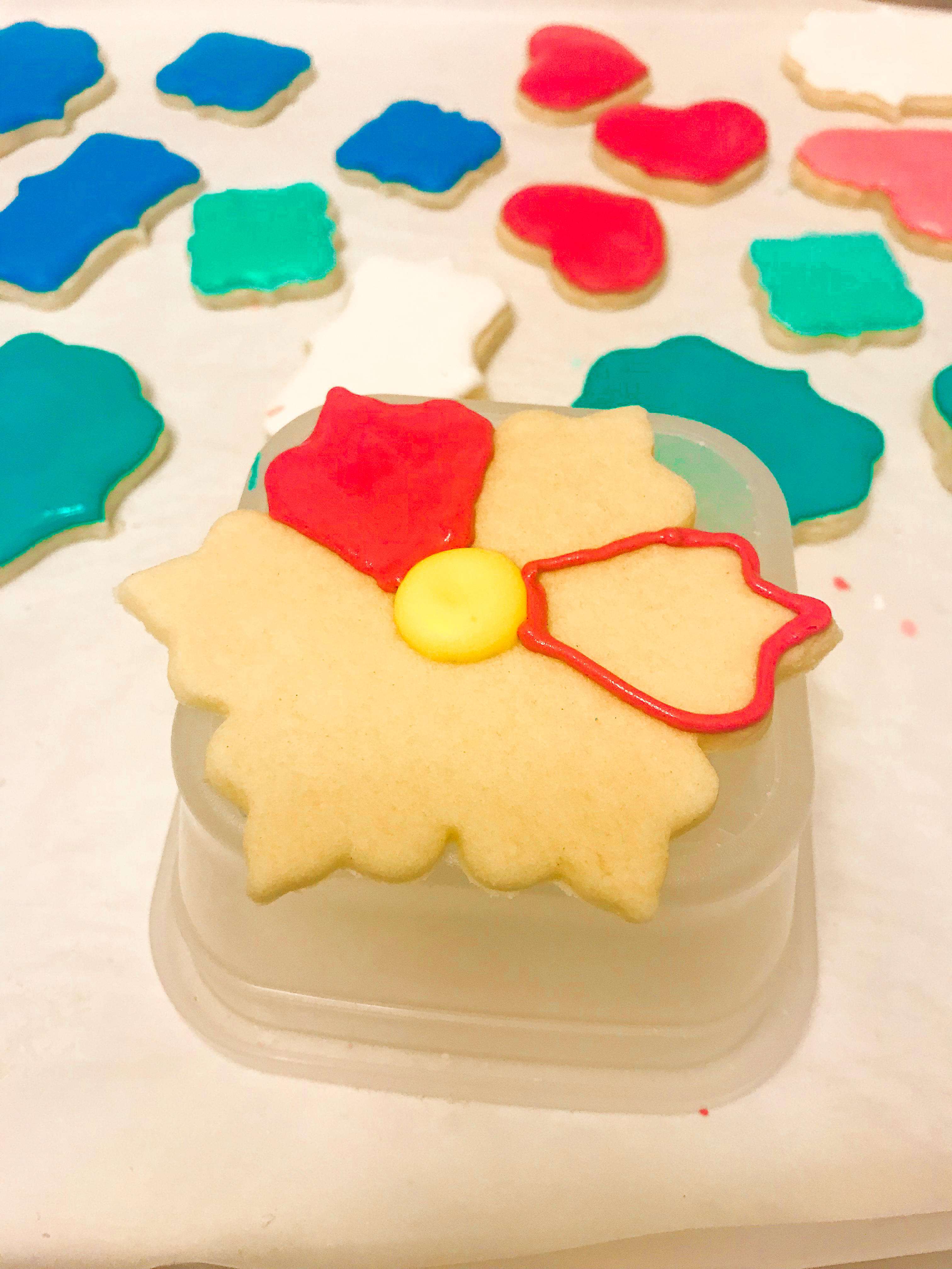 A partially decorated flower cookie surrounded by other royally iced cookies. 