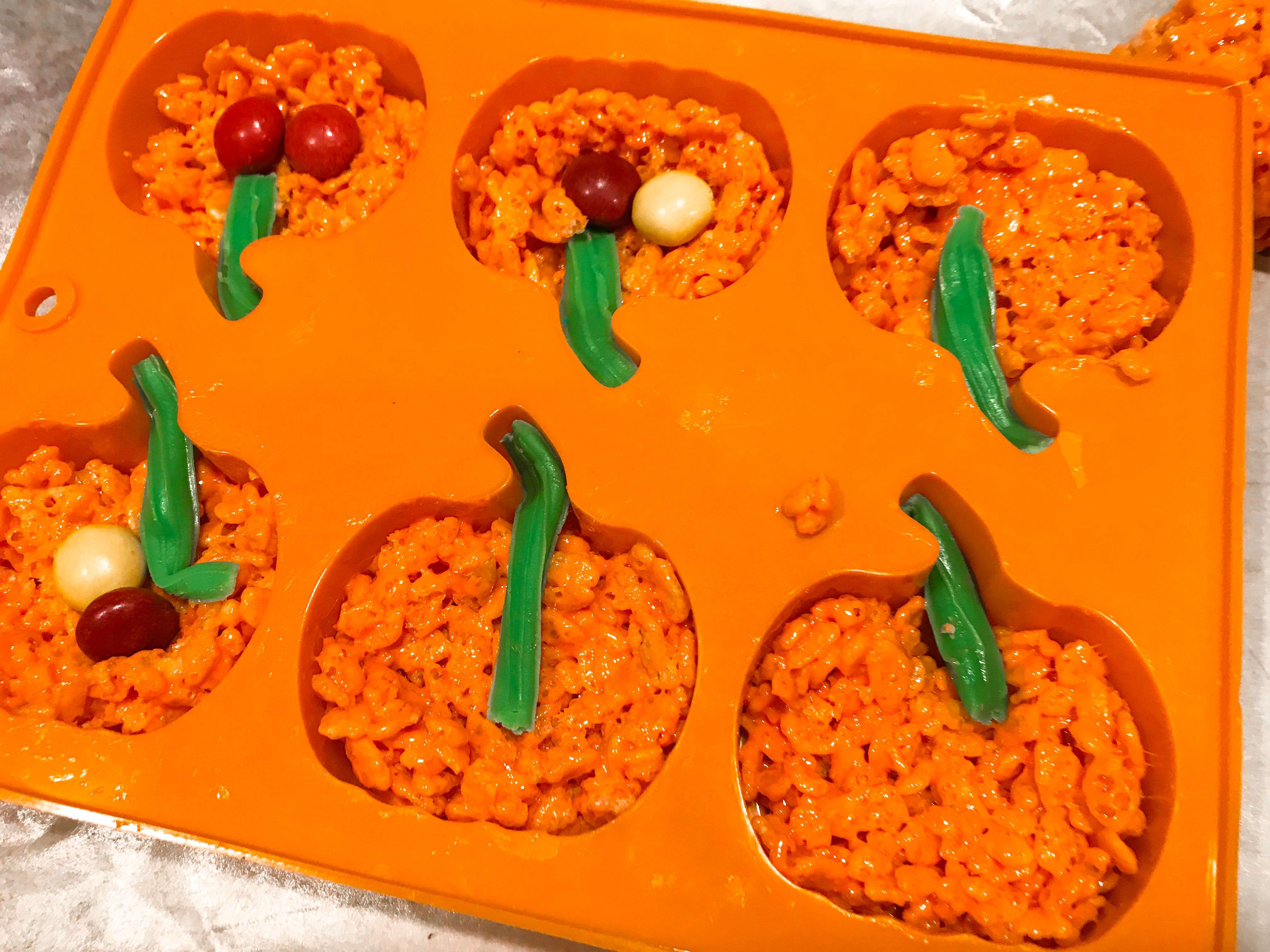Filling a pumpkin silicone mould with rice krispies and candy. 