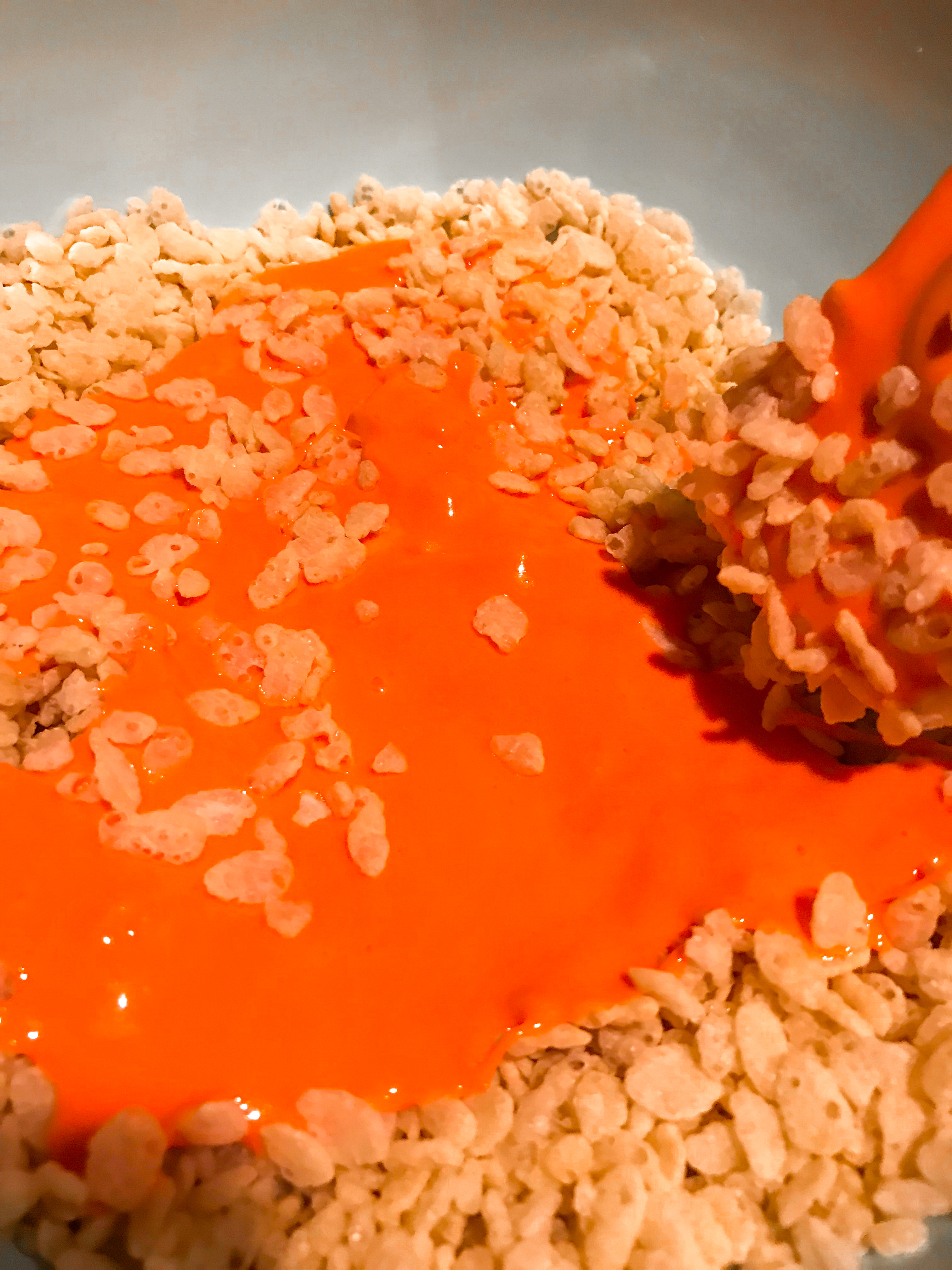 orange melted marshmallow being stirred into rice krispie cereal. 