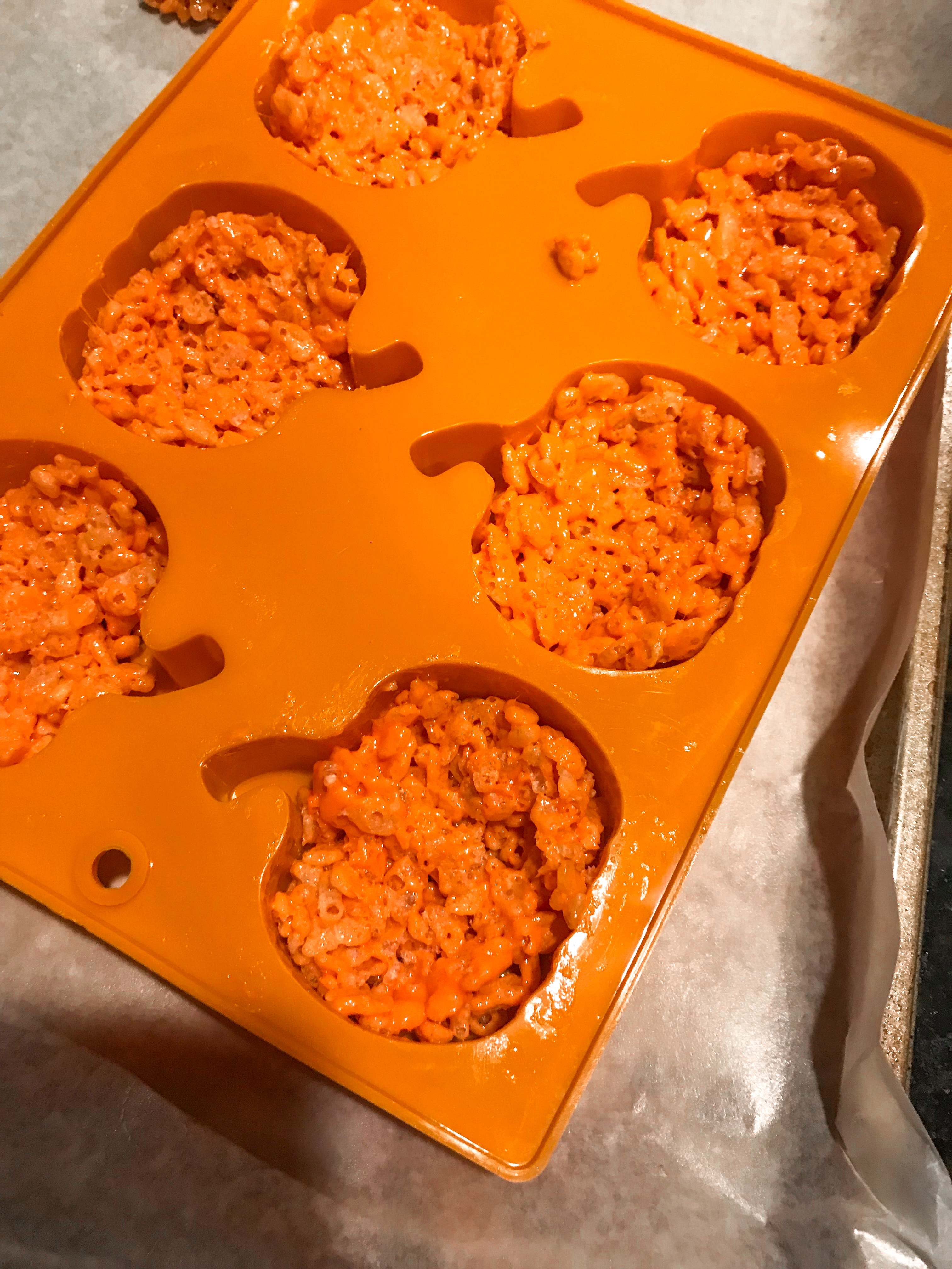 Orange rice krispie mix being pressed into a pumpkin mold.