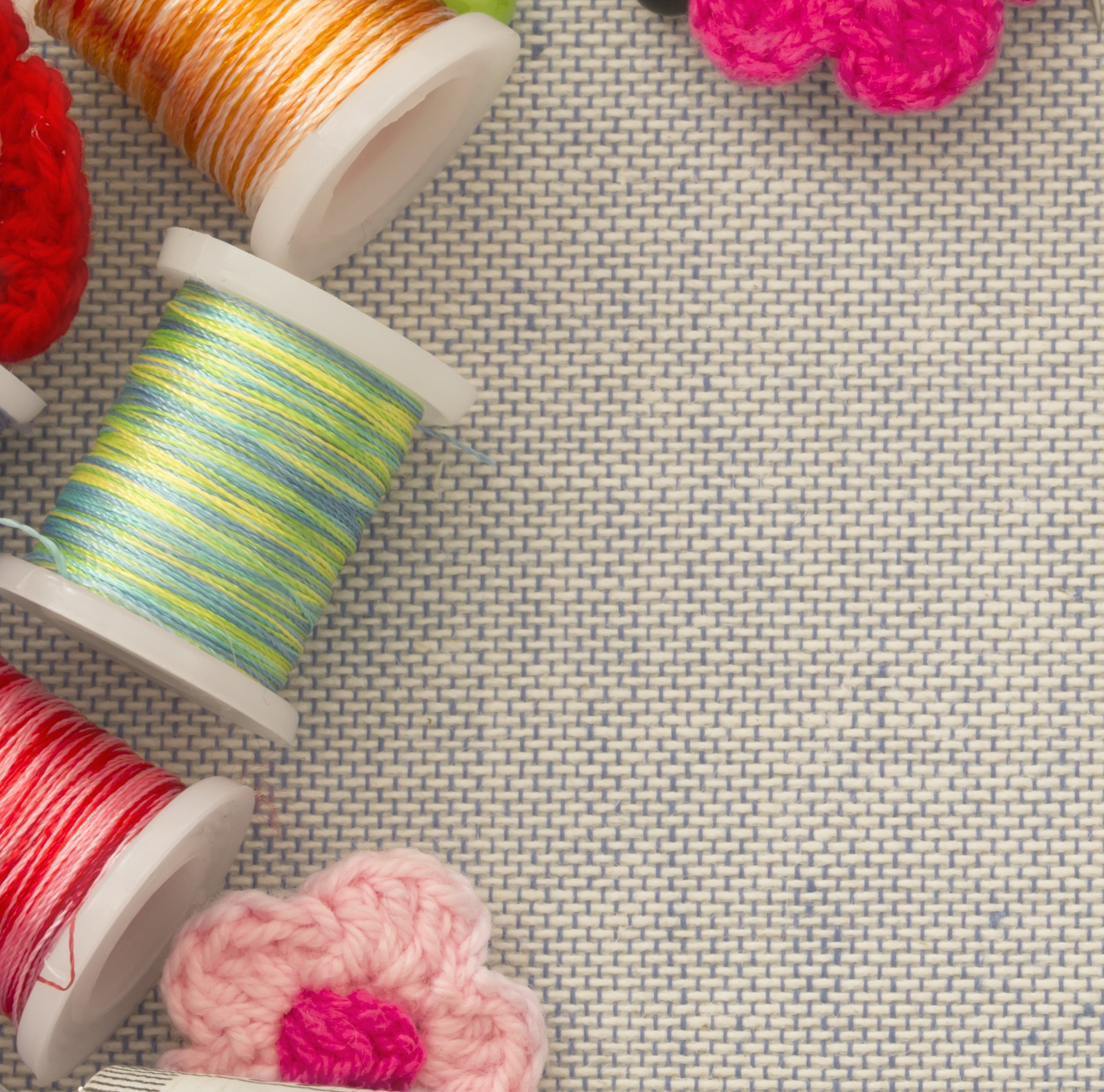 Spools of colorful thread and crocheted flowers on a burlap background