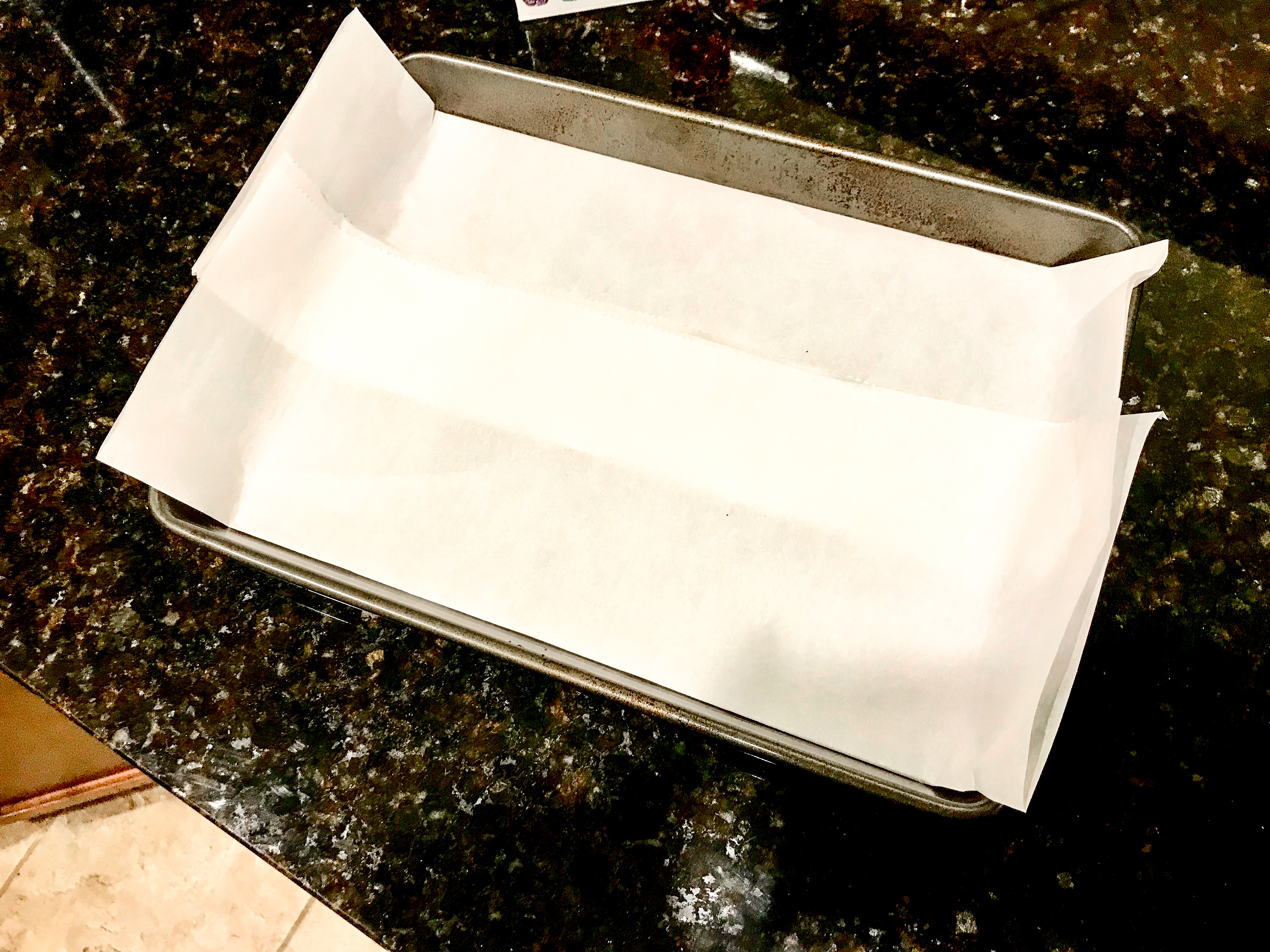 Folded parchment paper lining a metal baking dish. 