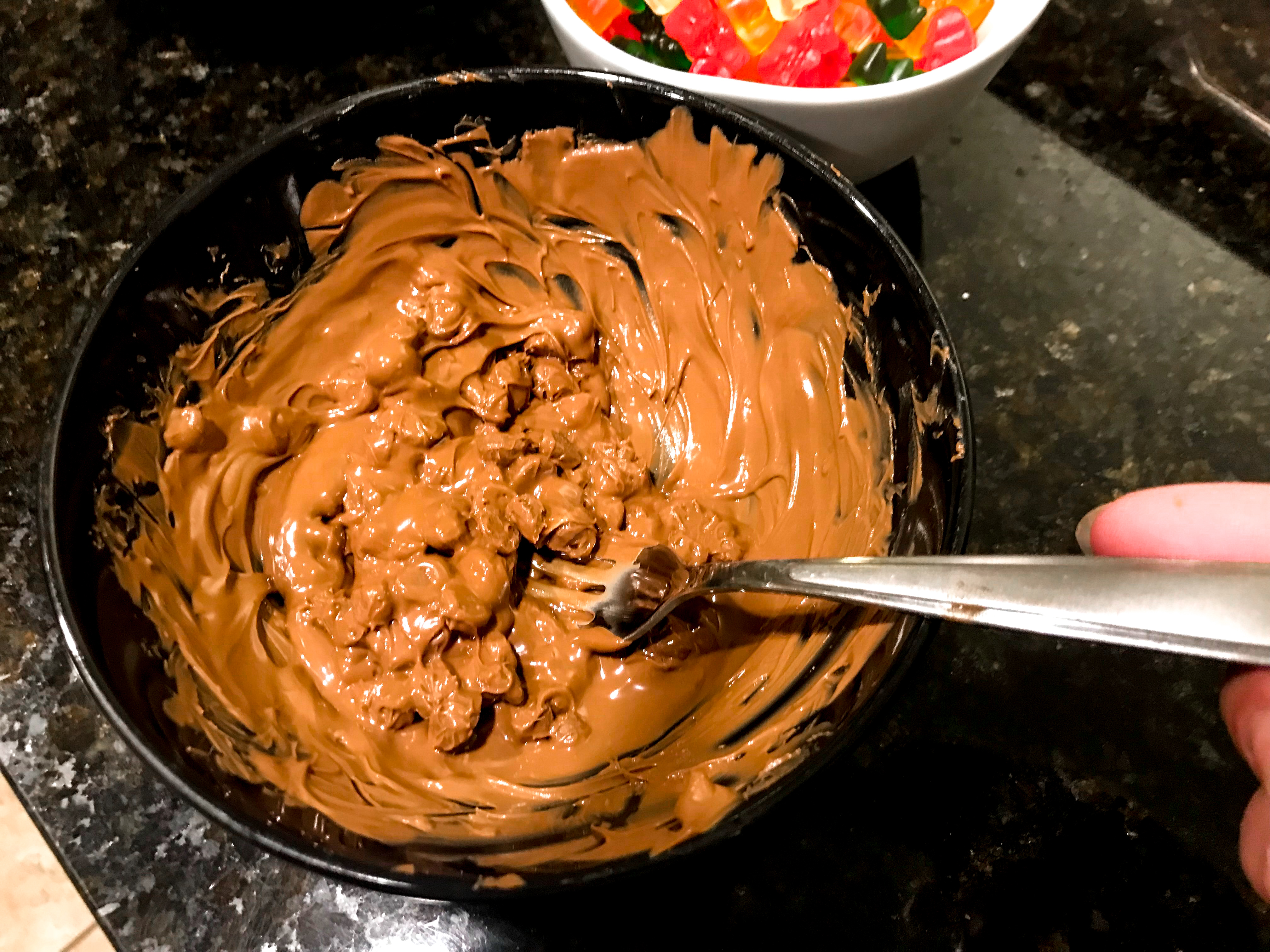 Partially melted chocolate in a bowl being stirred by a fork. 