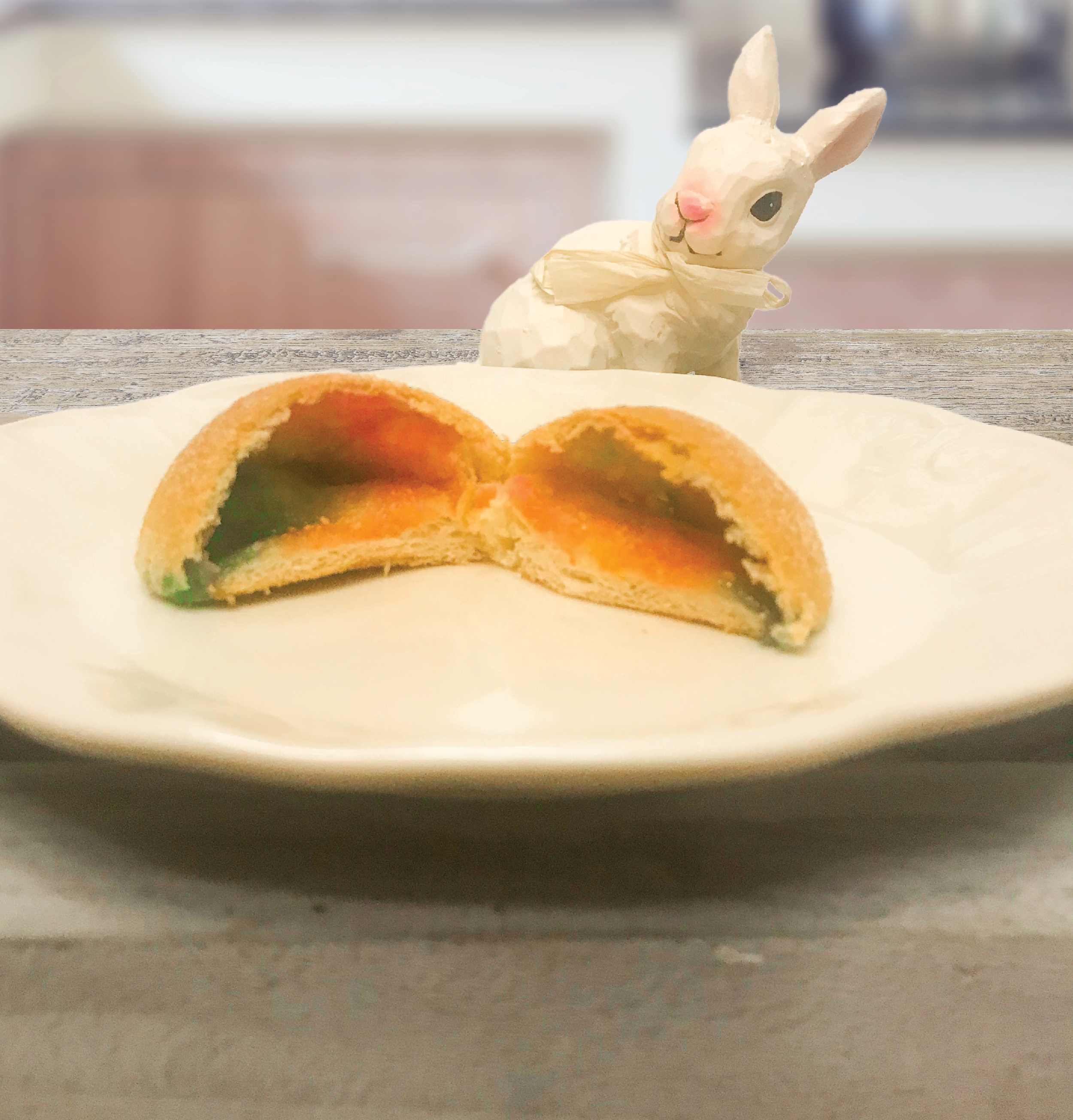 Hollow resurrection roll with colorful rainbow interior on a white platter in front of a ceramic bunny.