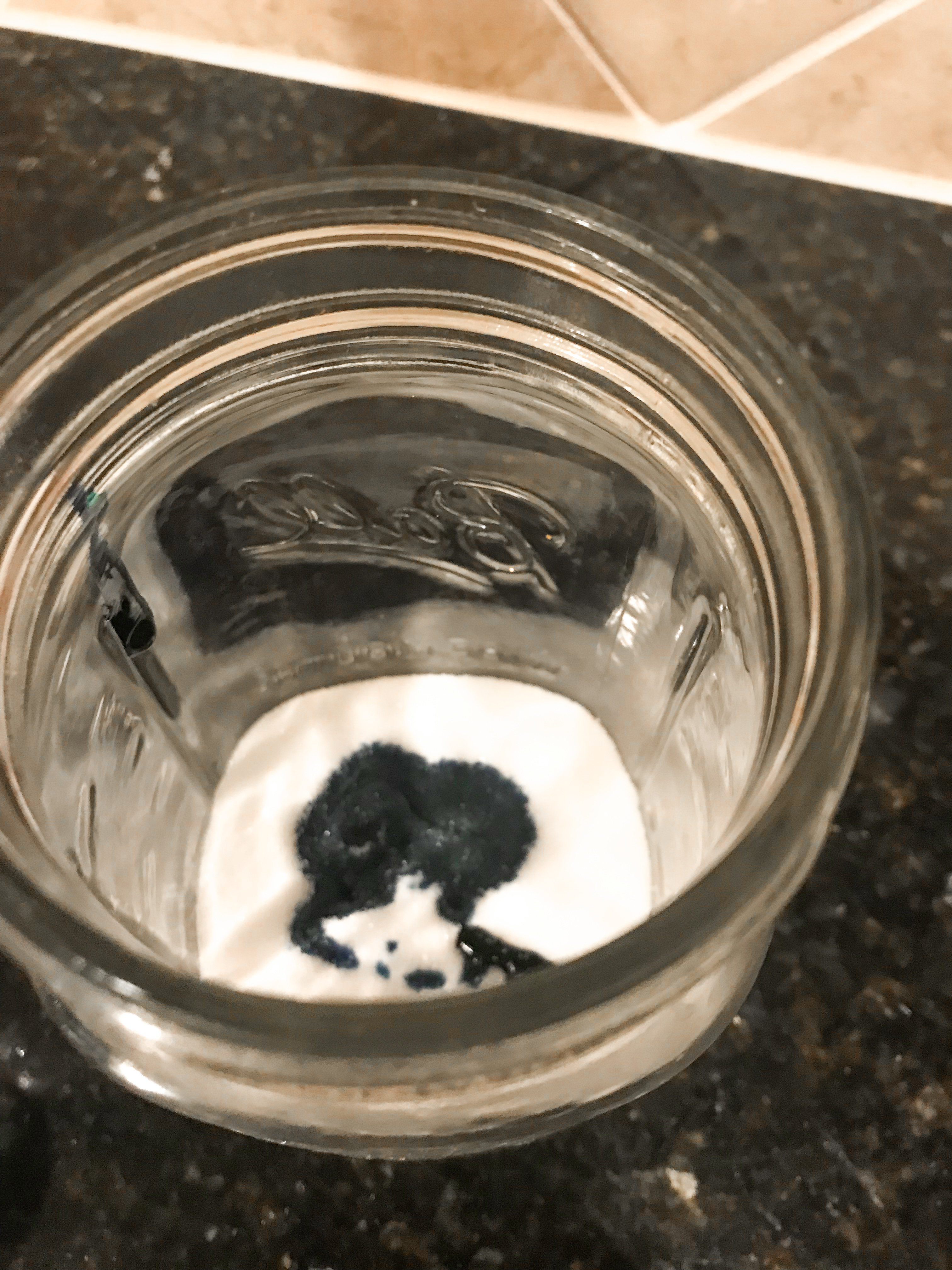 A mason jar with white sugar and spots of purple colored vodka.