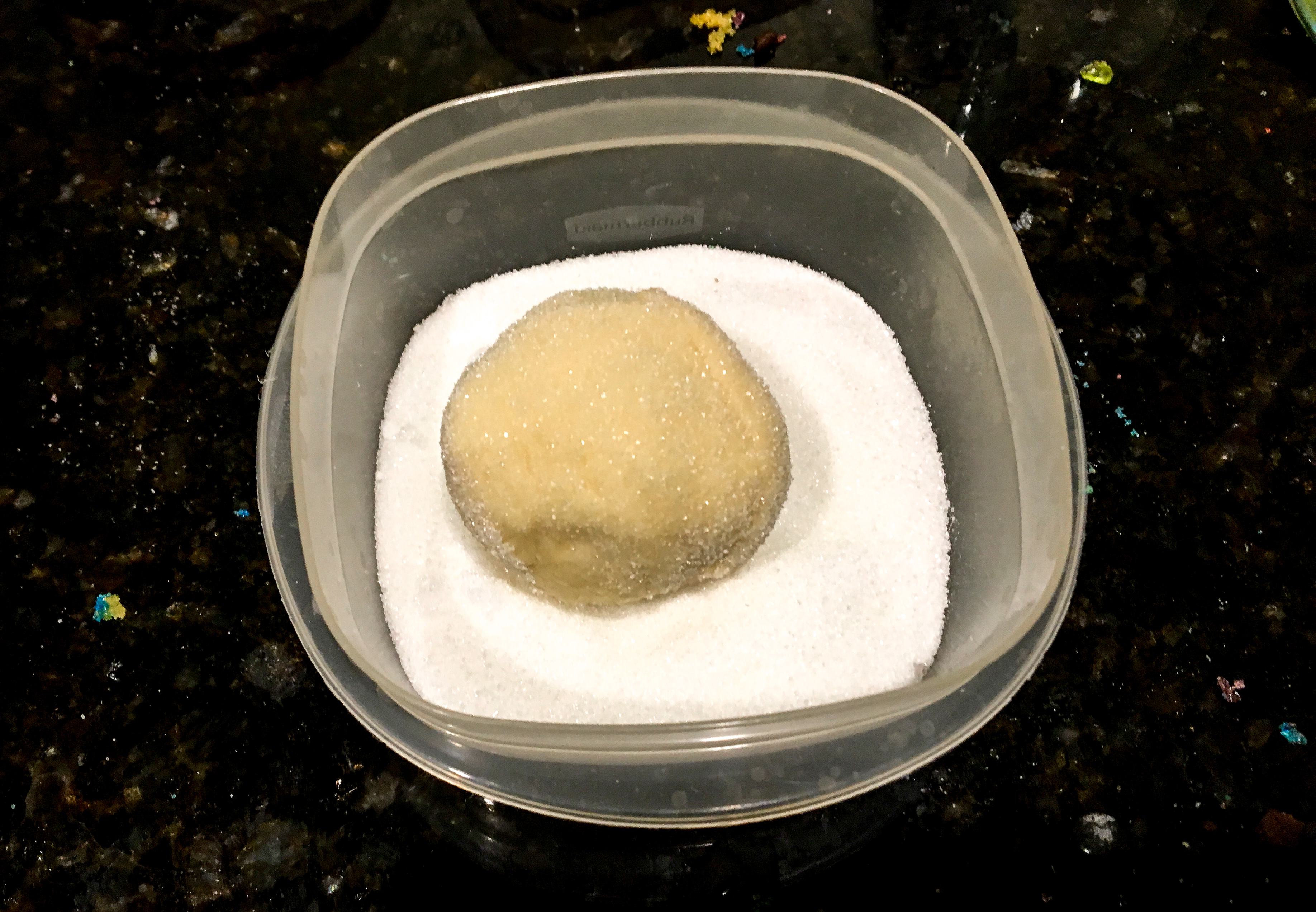 A ball of dough in a container full of white sugar on a countertop. 
