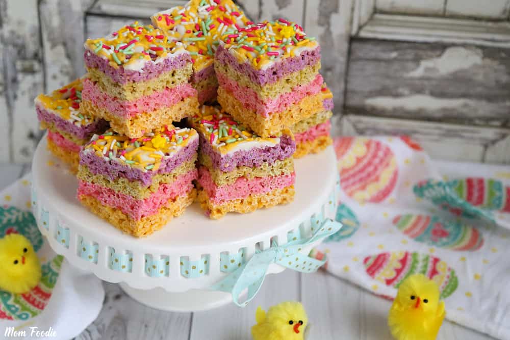 Large multi-layer pastel rice krispie treats on top of a platter surrounded by Easter decor. 
