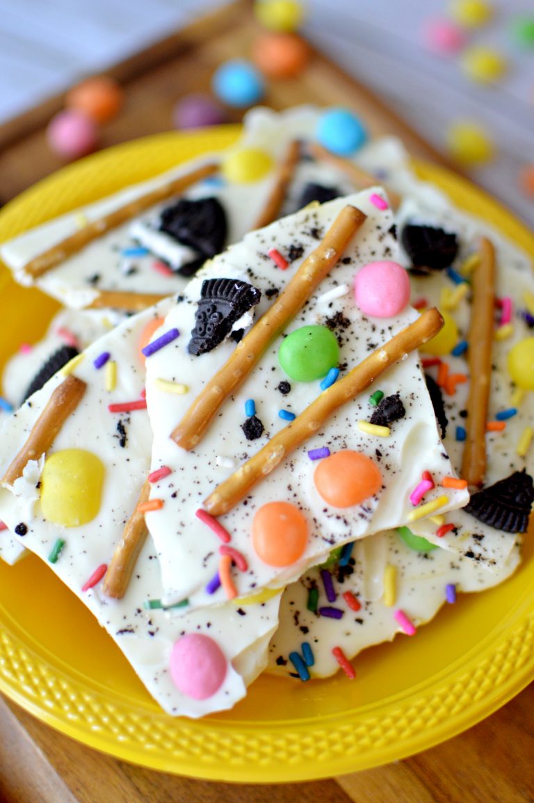 white chocolate bark containing pretzels and colorful candies on a yellow plate