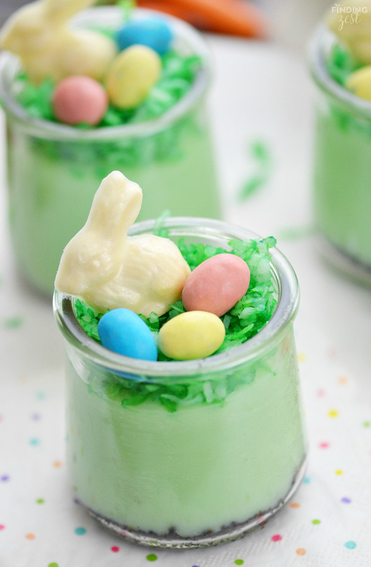 A small glass container holding green pudding, a white chocolate bunny and candies