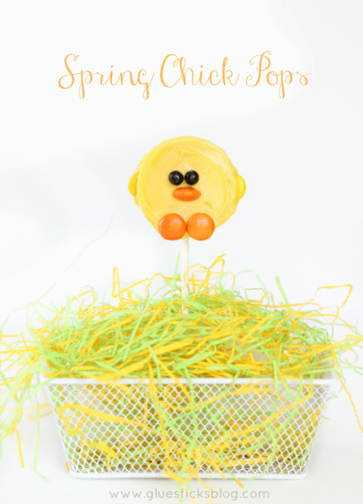 A single yellow chick oreo pop sticking out of a basket containing green and yellow raffia 