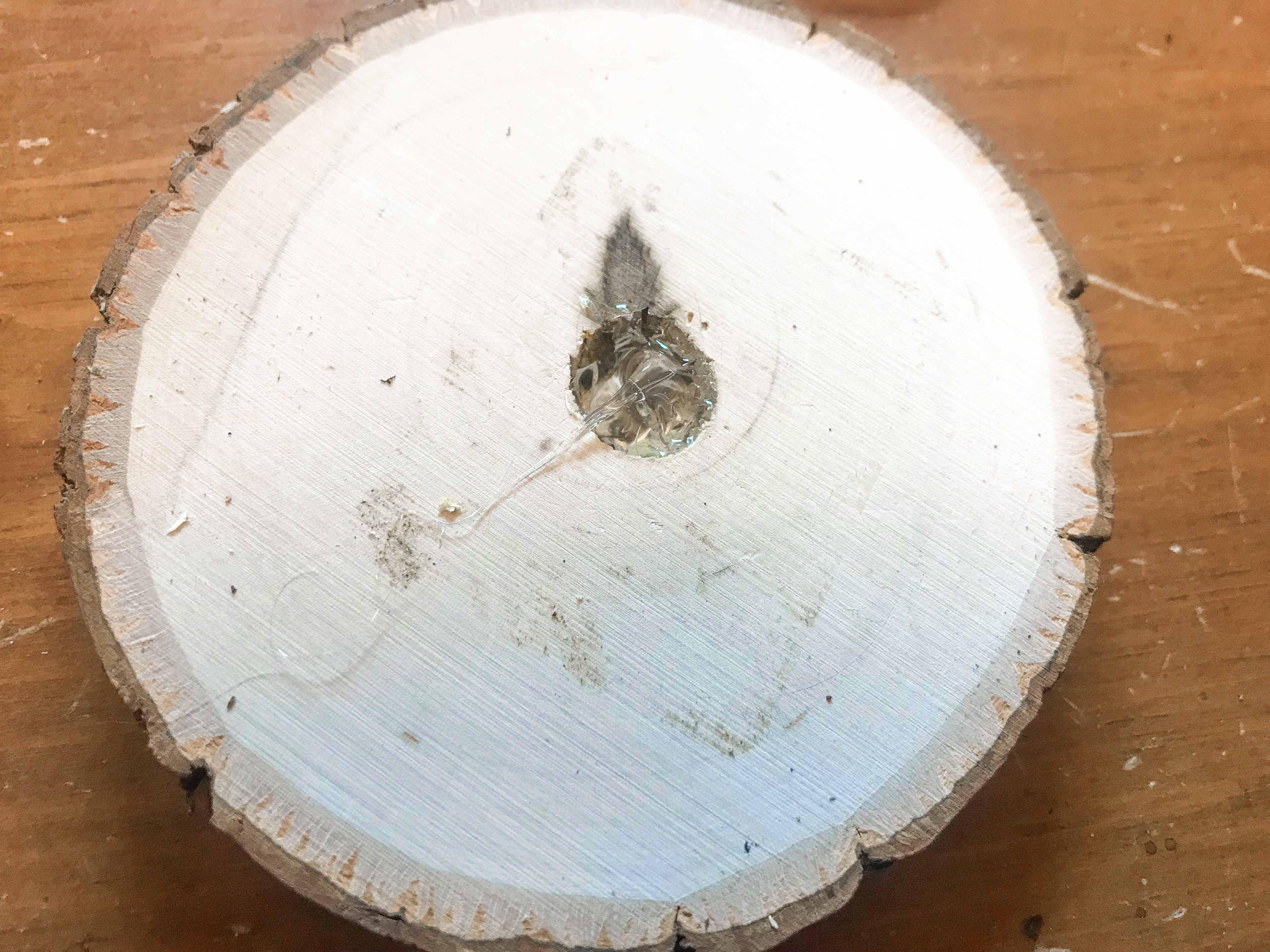 Round wood slice top side with large hole filled with hot glue.
