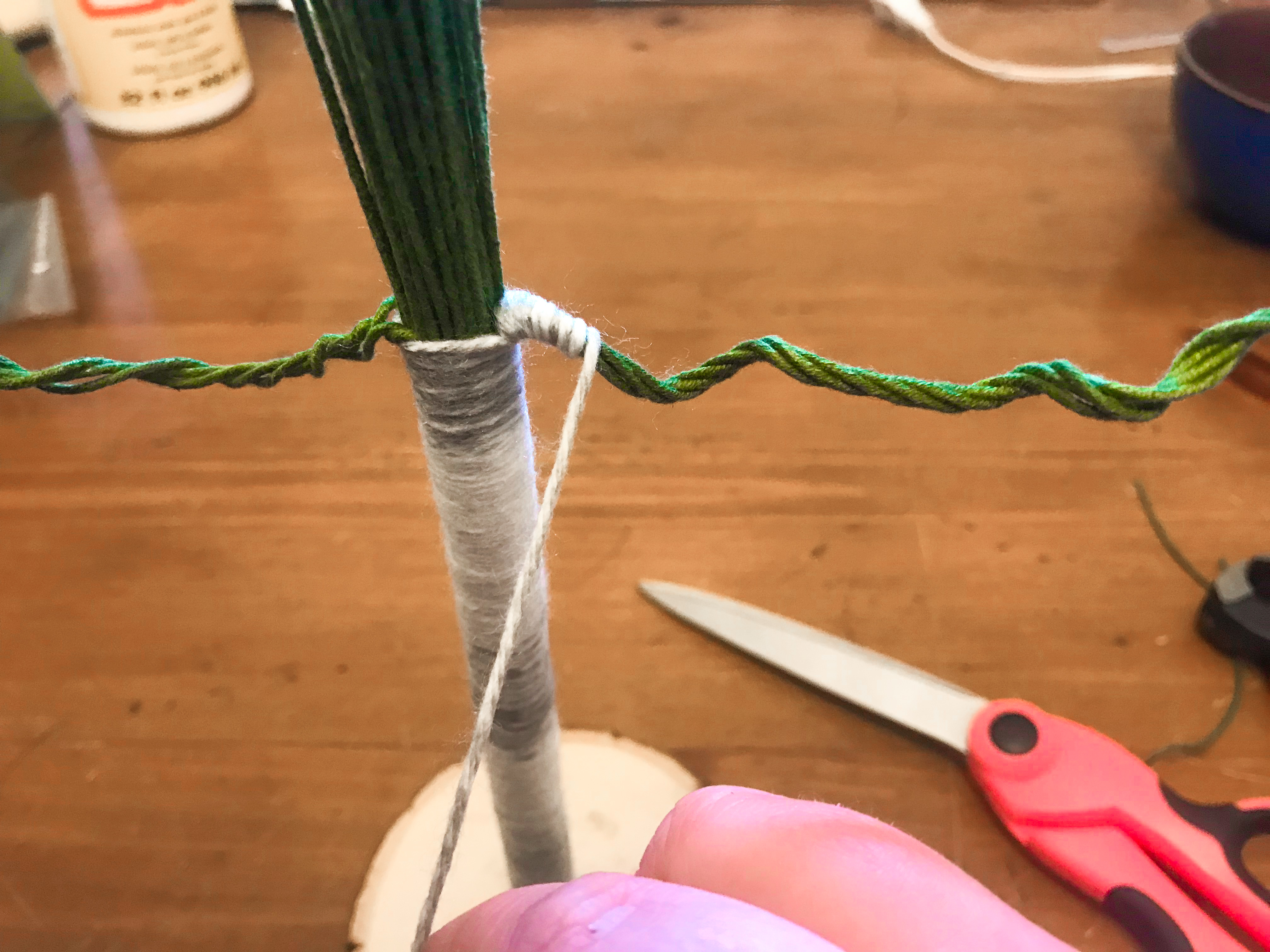 Yarn being tightly wrapped along floral stem branch jutting from yarn wrapped trunk. 