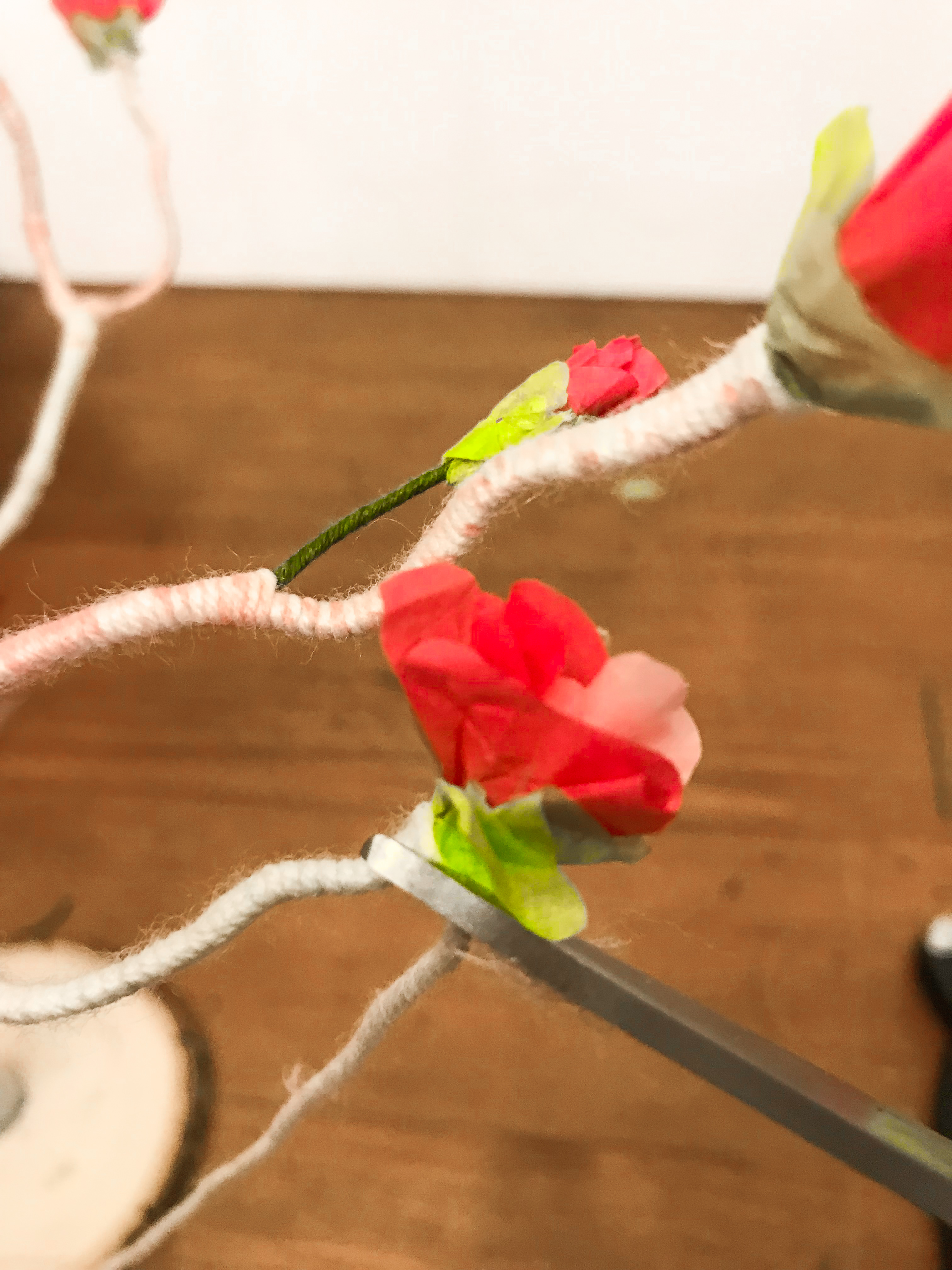 Scissors cutting yarn at the overlap point with tissue paper flowers. 