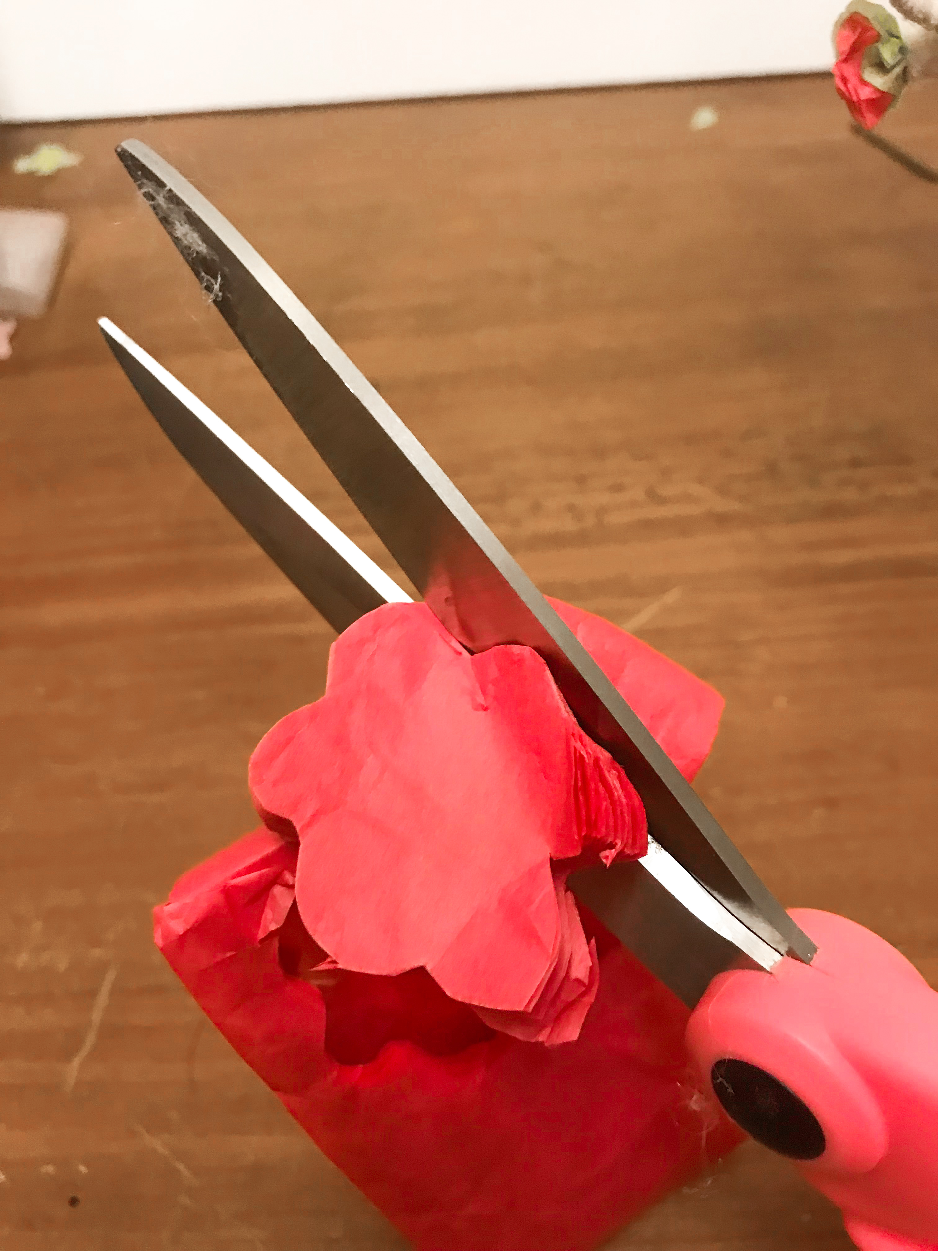 Pink scissors cutting out 6 petaled flower shape from hot pink folded tissue paper