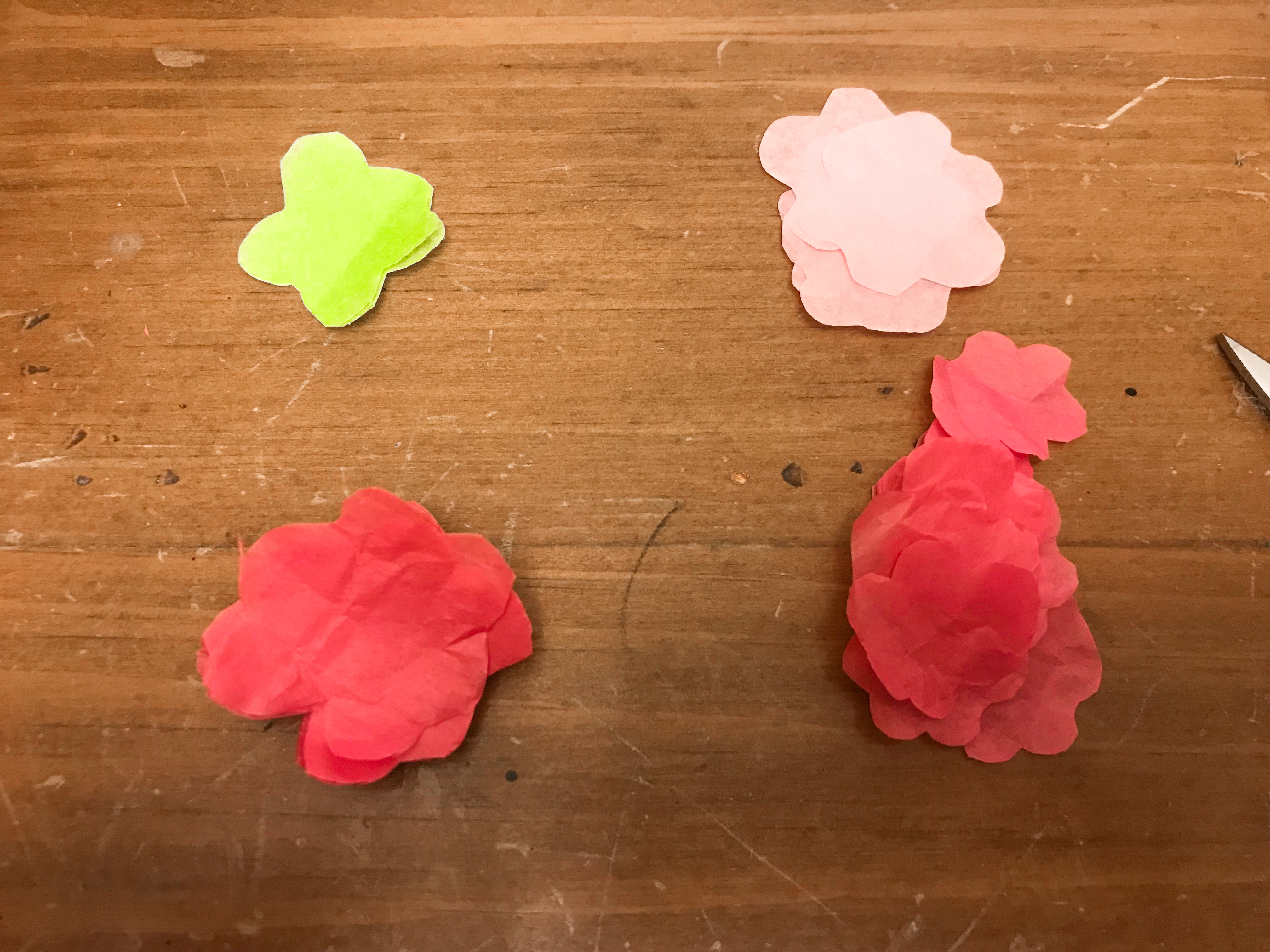 Green, light pink, and hot pink flower shaped tissue paper cut-outs on a wood background