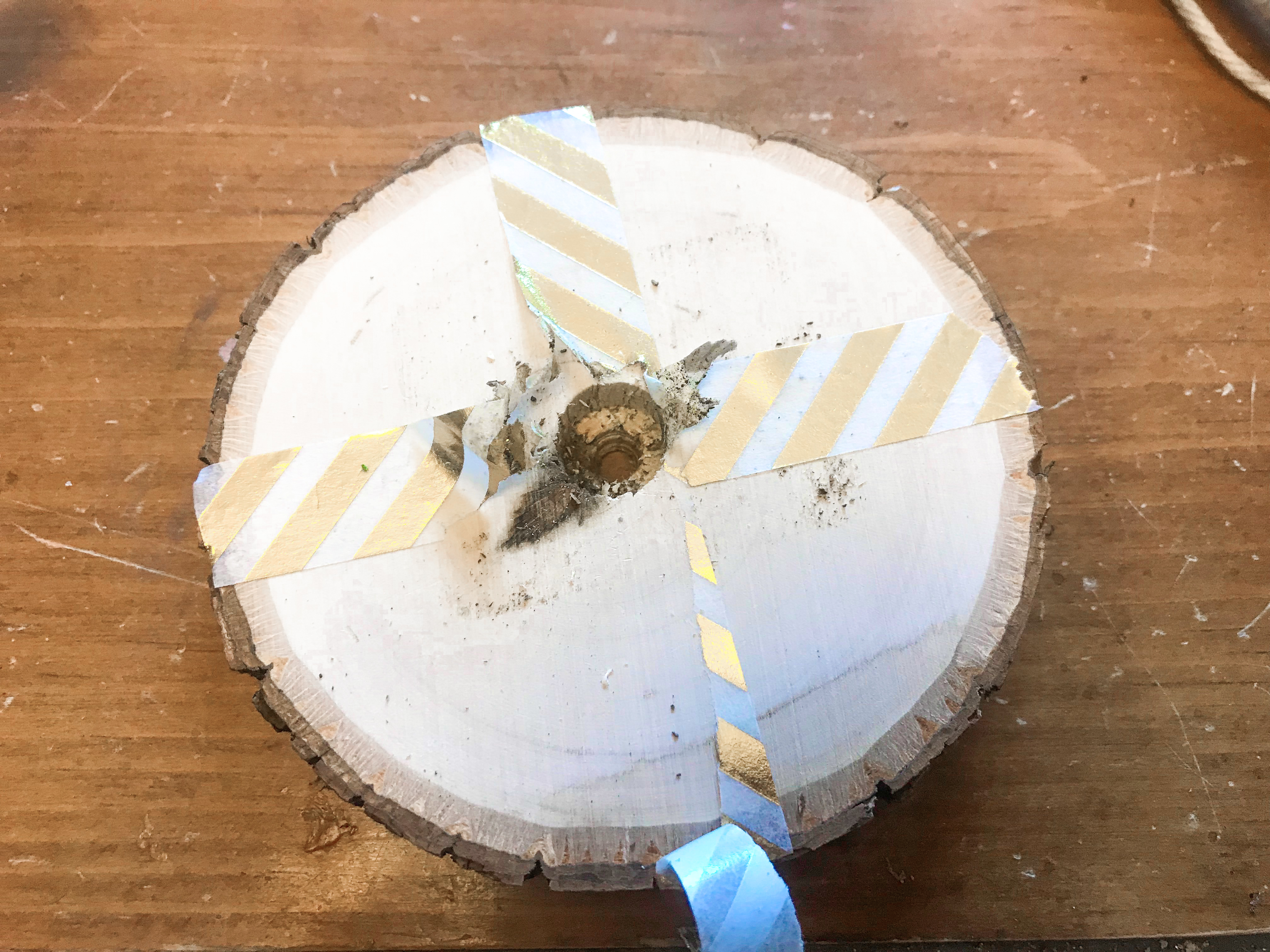 Round wood slice with a drilled hole in the center surrounded by peeling gold washi tape. 