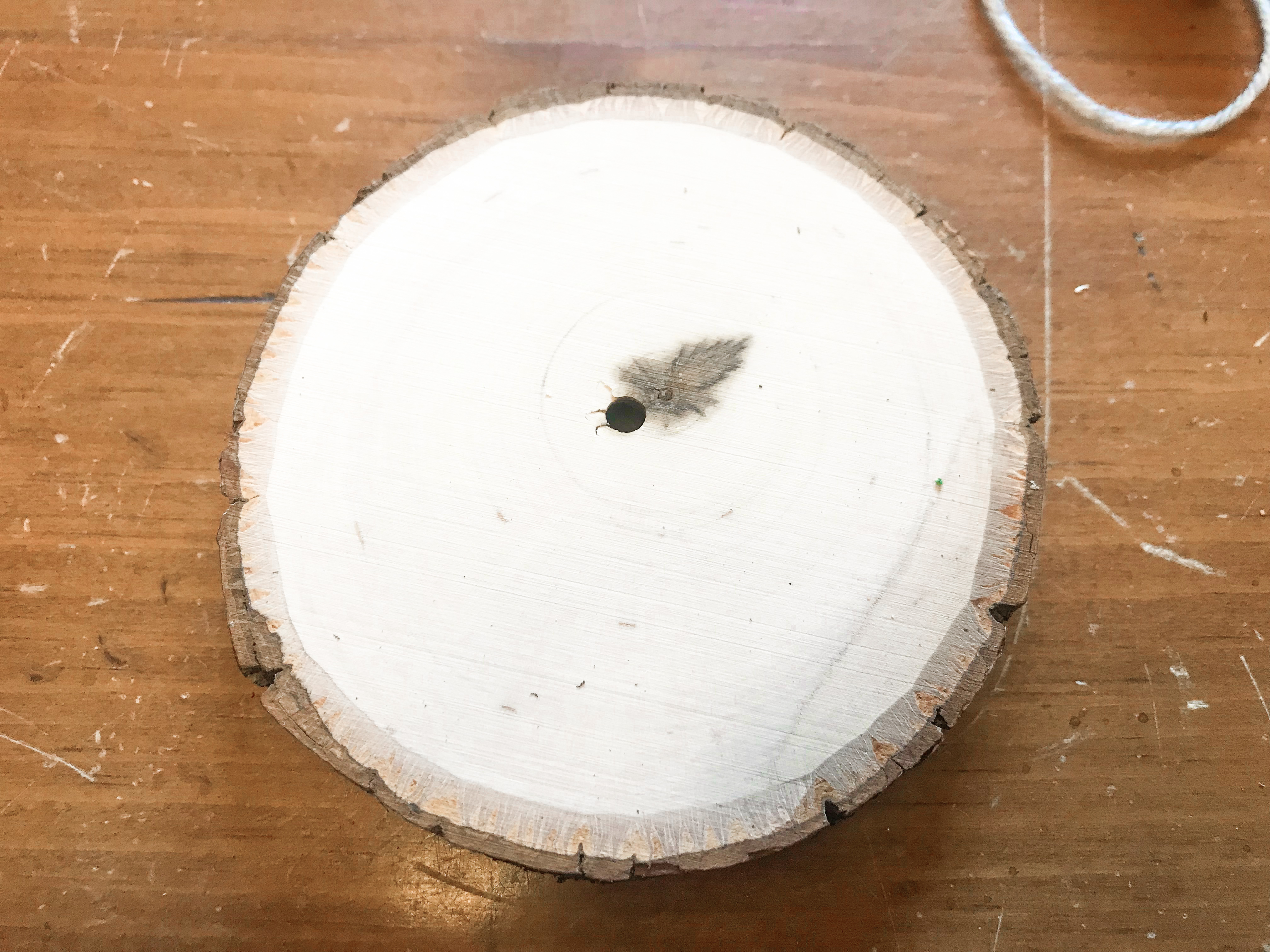 Underside of round wood slice with small hole drilled in the center on a wood background
