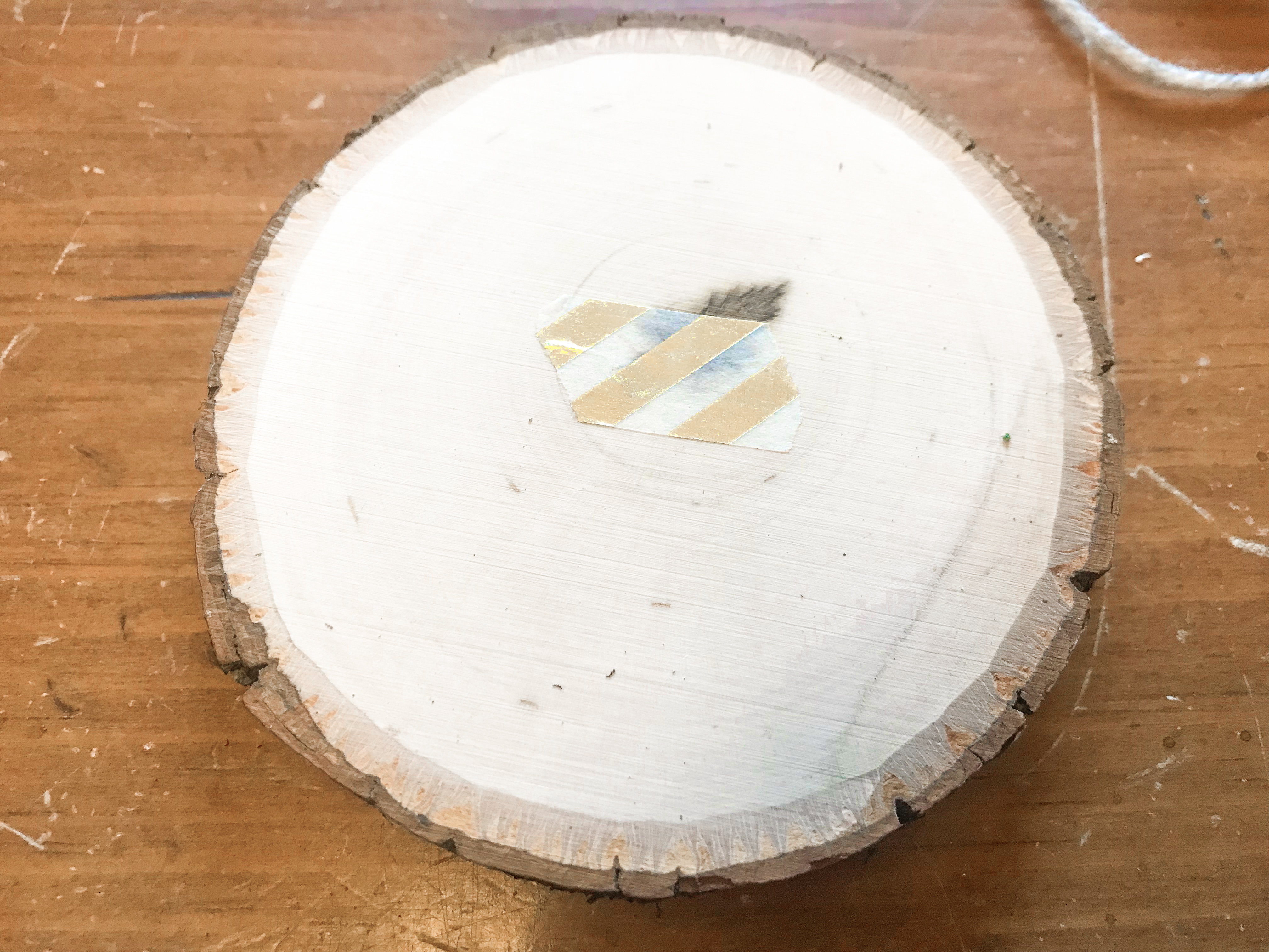 Underside of a round wood slice with gold washi tape covering the small drilled hole 