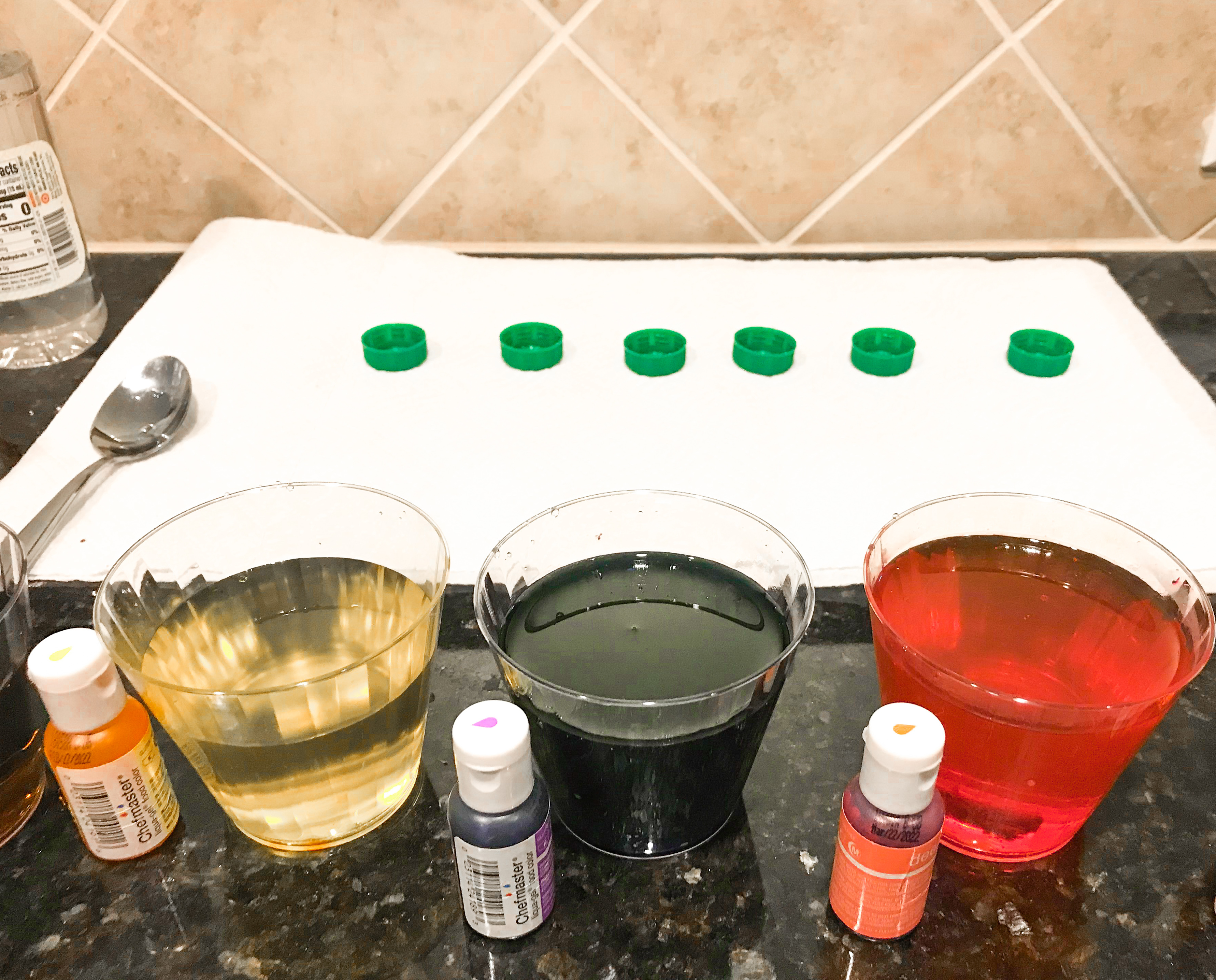 Glasses of Easter egg dye, food coloring, and bottle caps on a paper towel. 