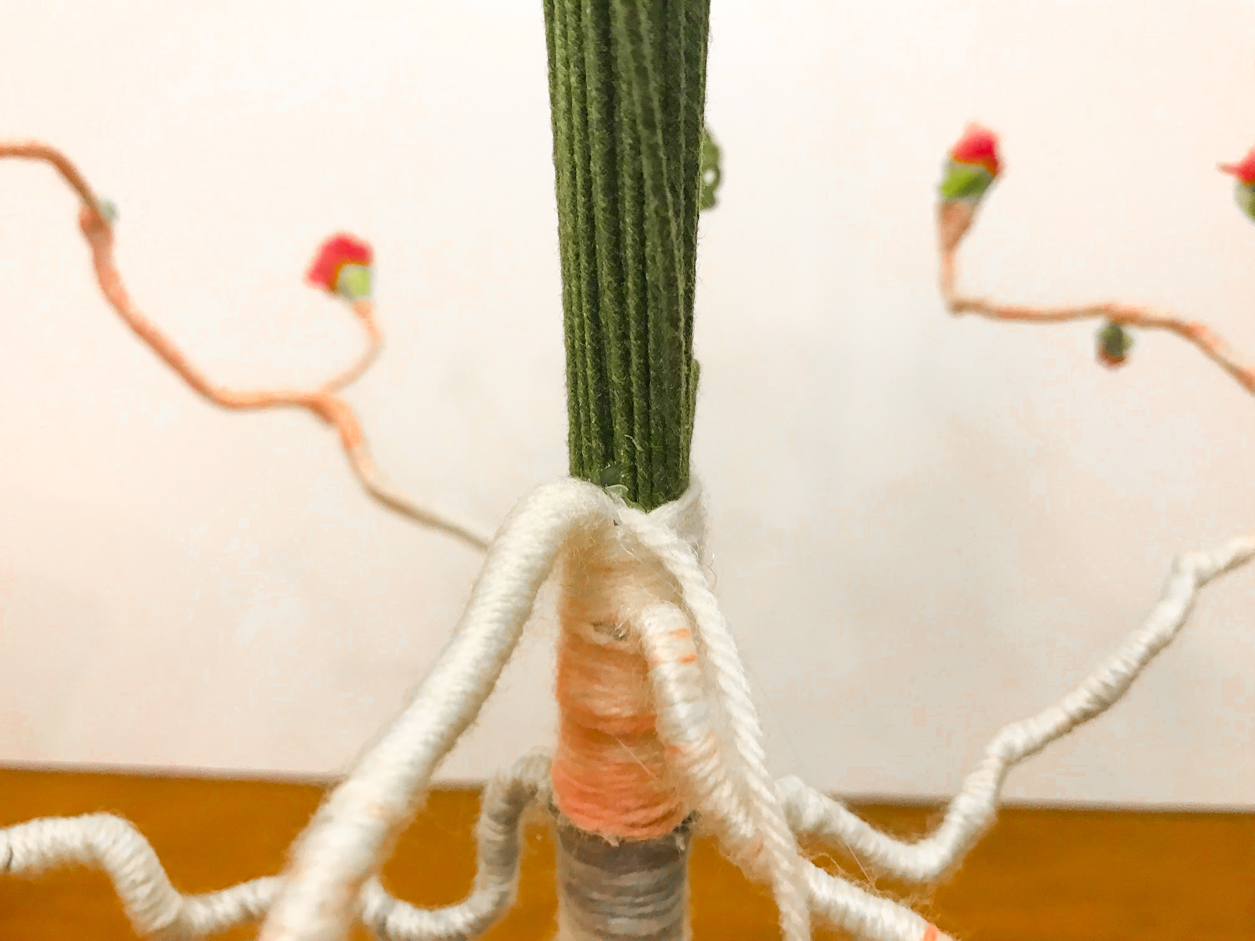 Yarn pushed into hot glue at junction of yarn wrapped branch and unwrapped floral stem trunk.