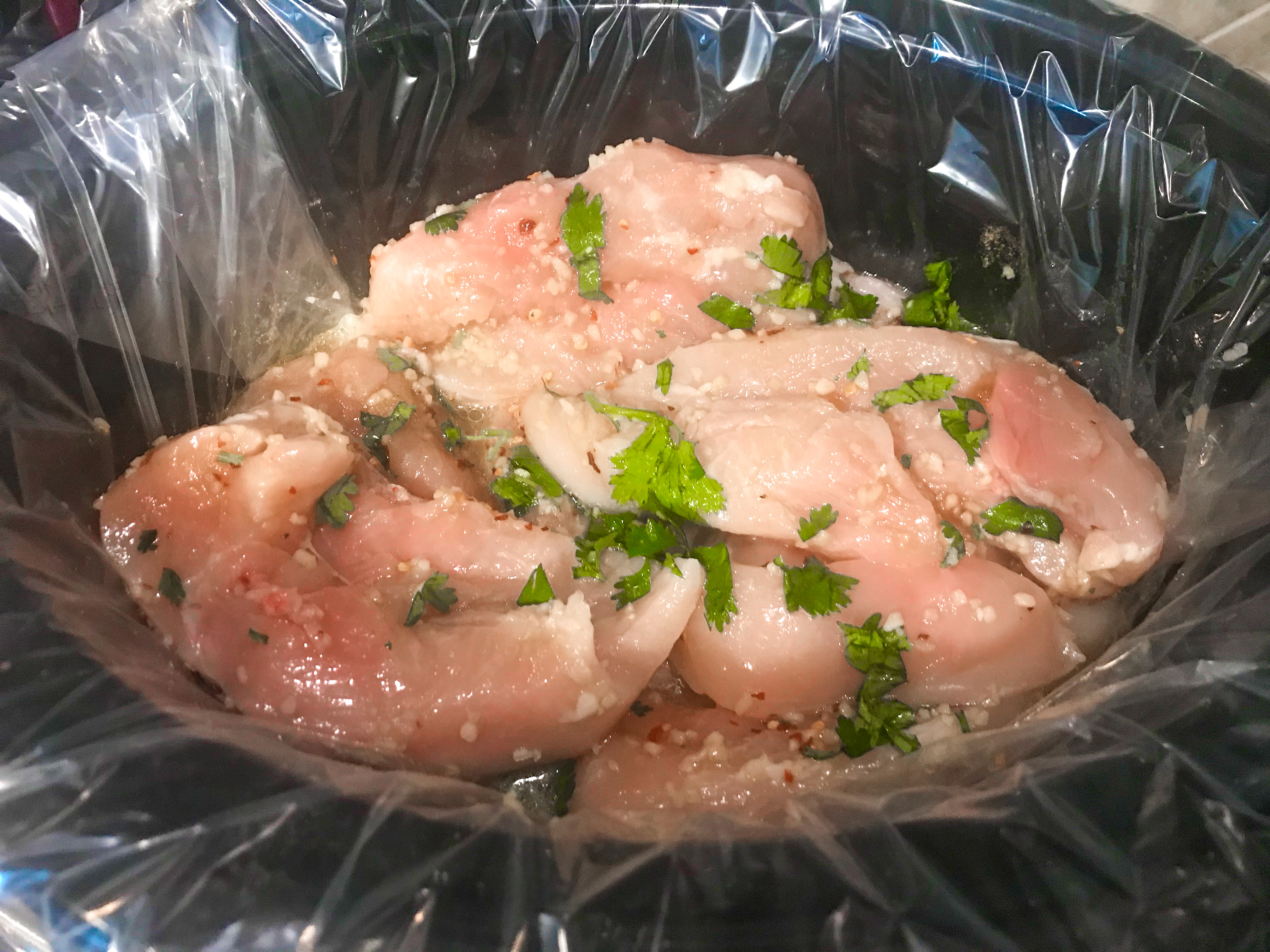 Raw chicken and seasonings in a lined crockpot. 
