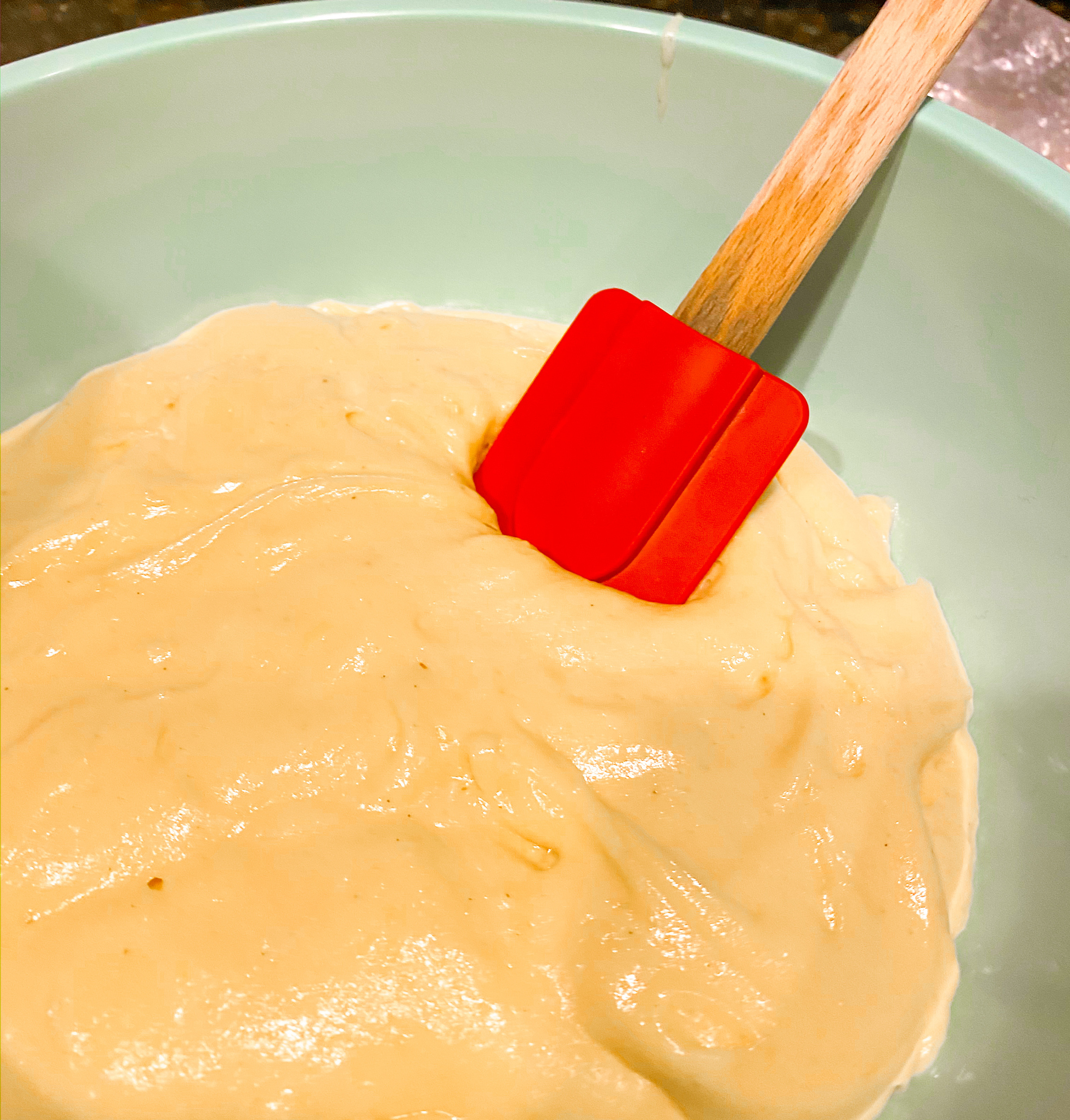 Yellow bundt cake mix in a bowl with a red spatula. 